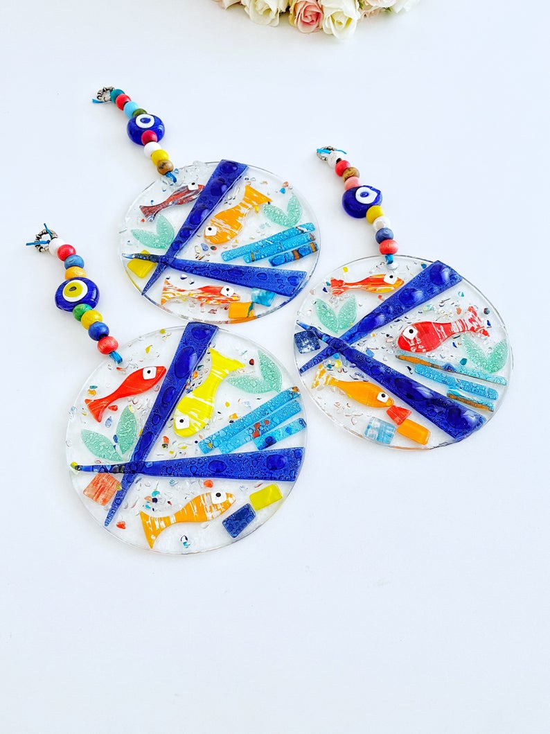 A vibrant Fish Evil Eye Wall Hanging made of fused glass, featuring a unique design with a protective evil eye motif, measuring 12cm x 12cm.