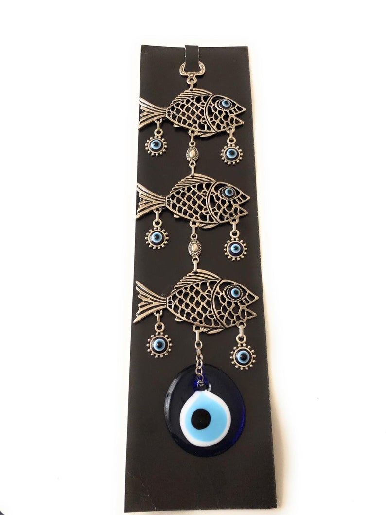 A decorative fish wall hanging featuring blue evil eye beads, crafted with metal charms, symbolizing good luck and protection.