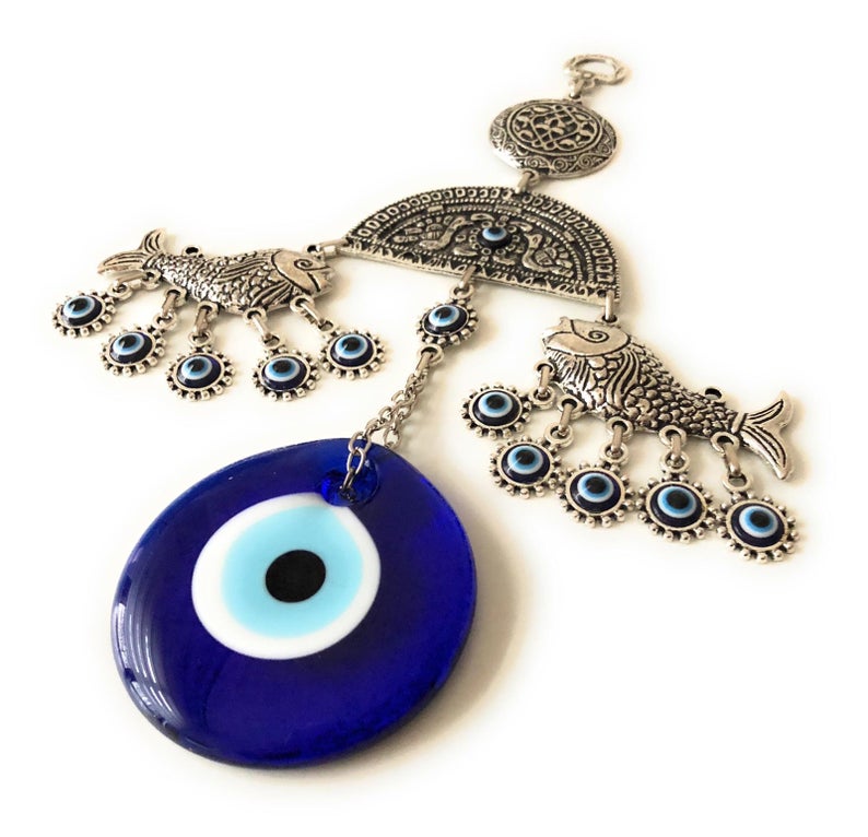 A decorative fish wall hanging featuring blue evil eye beads, crafted with metal charms, symbolizing good luck and protection.