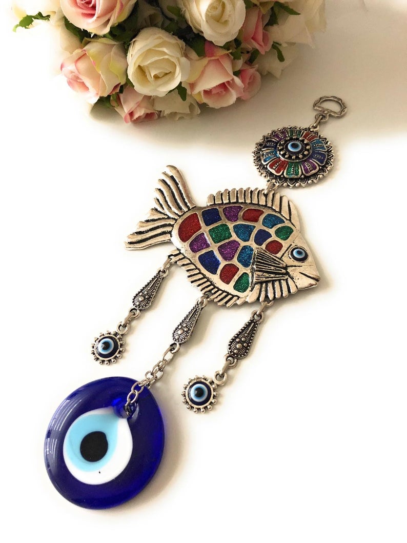 A decorative fish wall hanging featuring blue evil eye beads, crafted with metal charms, symbolizing good luck and protection.