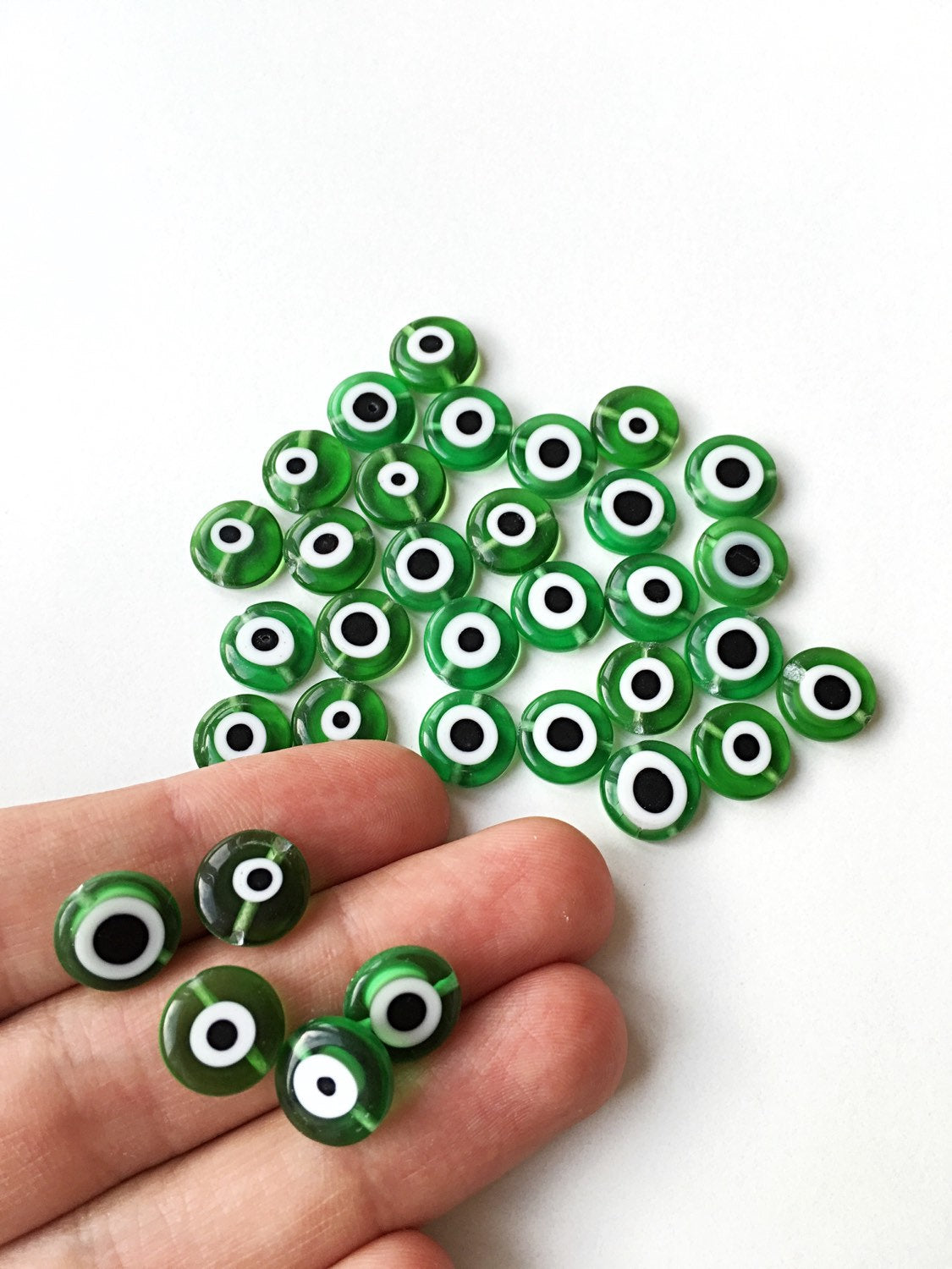 A collection of green flat evil eye glass beads in various sizes from 6mm to 12mm, showcasing their unique designs and vibrant color.