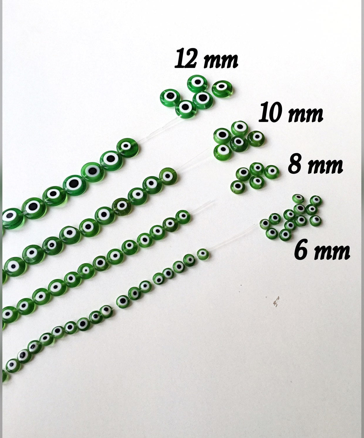 A collection of green flat evil eye glass beads in various sizes from 6mm to 12mm, showcasing their unique designs and vibrant color.