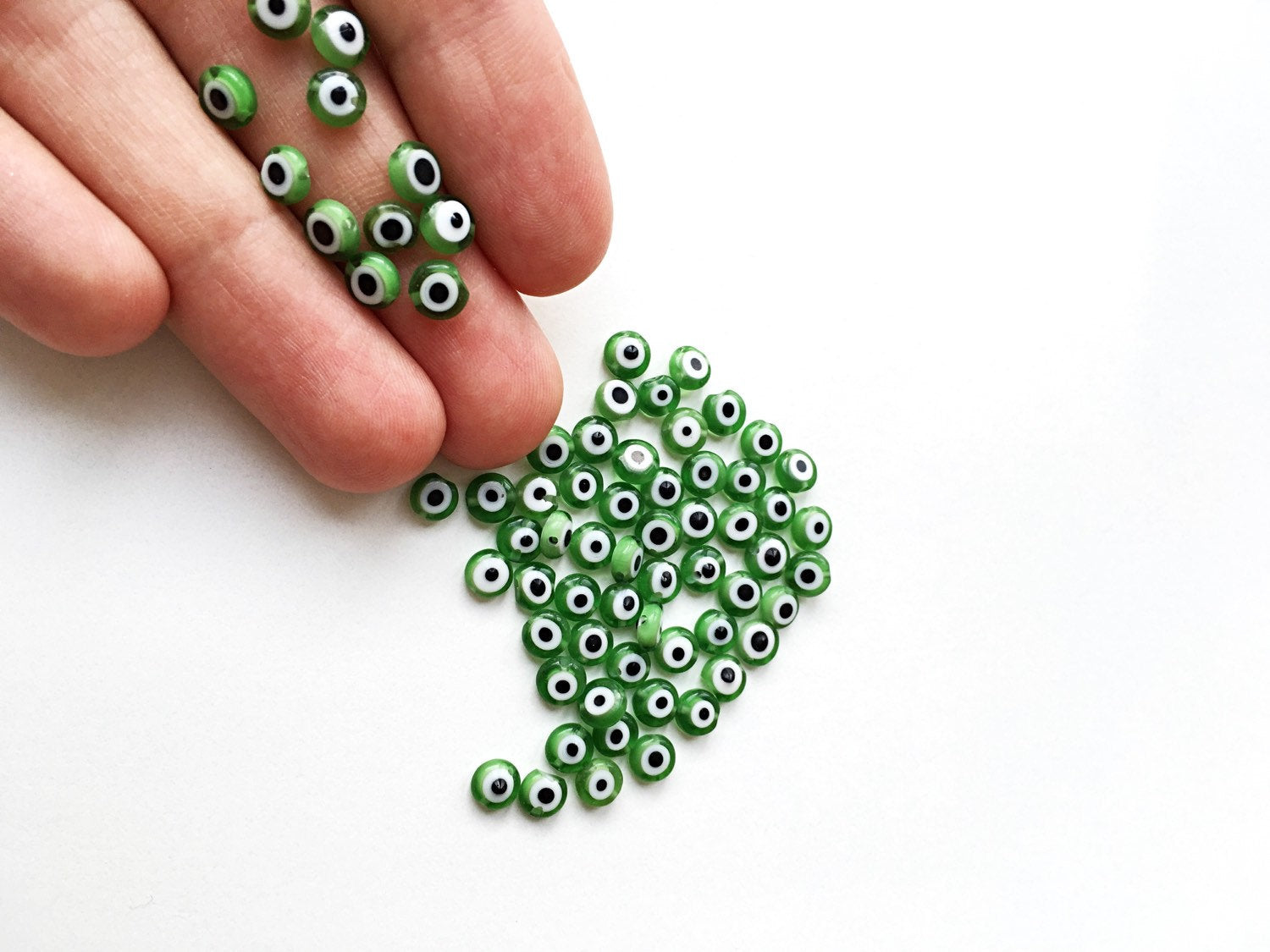 A collection of green flat evil eye glass beads in various sizes from 6mm to 12mm, showcasing their unique designs and vibrant color.