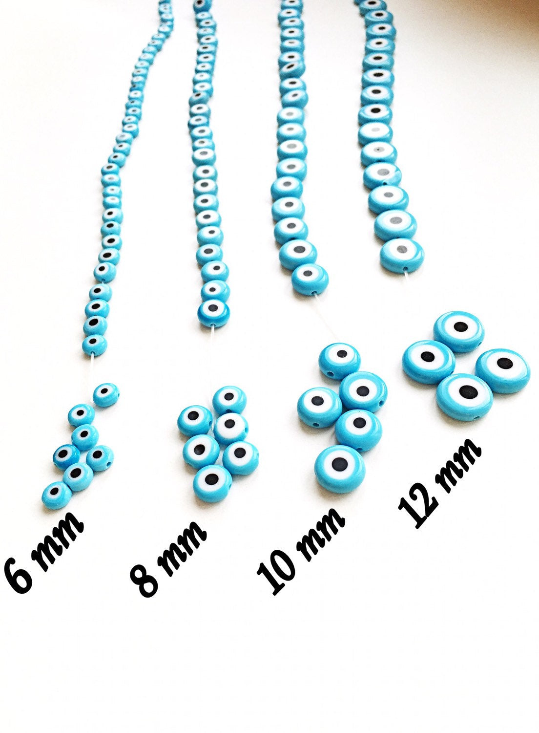 Flat evil eye glass beads in tale turquoise, ranging from 6mm to 12mm, displayed on a hand.