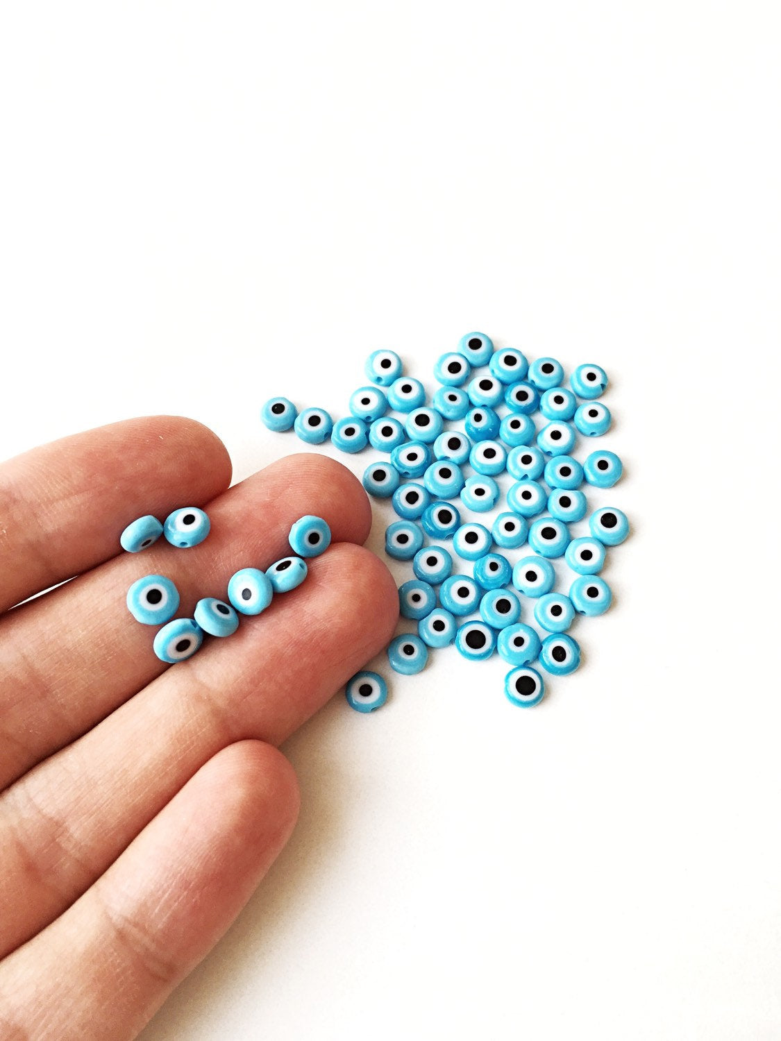 Flat evil eye glass beads in tale turquoise, ranging from 6mm to 12mm, displayed on a hand.