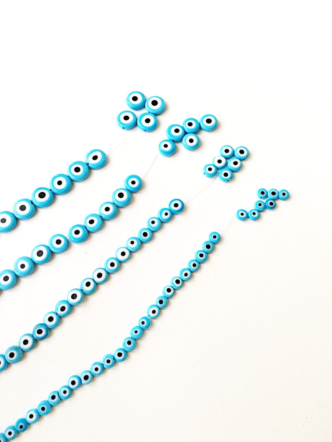 Flat evil eye glass beads in tale turquoise, ranging from 6mm to 12mm, displayed on a hand.