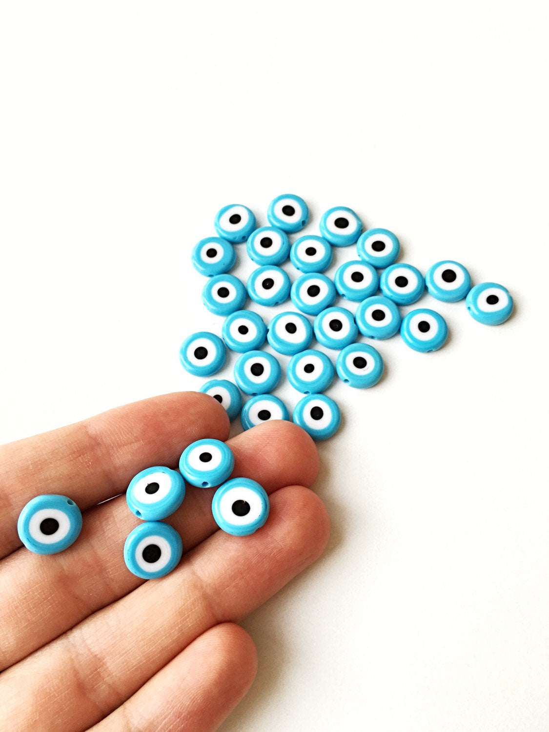 Flat evil eye glass beads in tale turquoise, ranging from 6mm to 12mm, displayed on a hand.