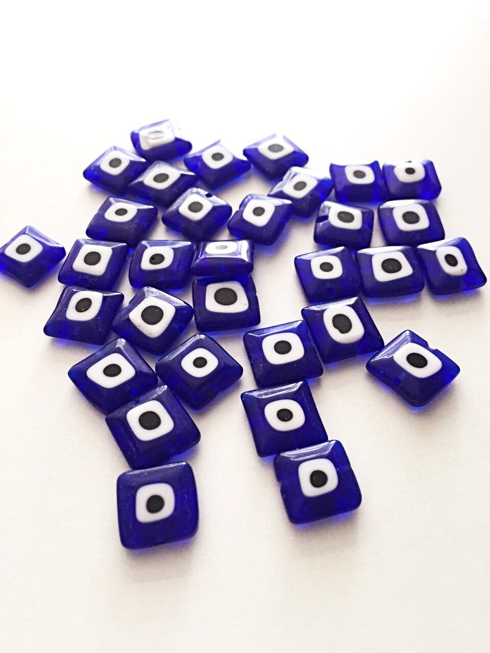 A collection of 10mm flat square glass evil eye beads in turquoise and dark blue, showcasing their unique design and color.