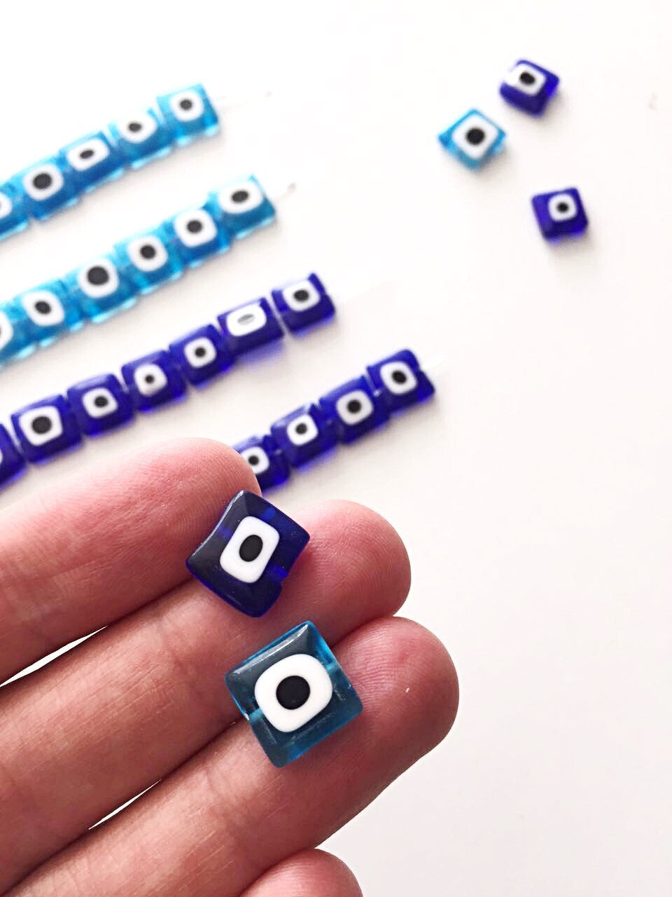 A collection of 10mm flat square glass evil eye beads in turquoise and dark blue, showcasing their unique design and color.