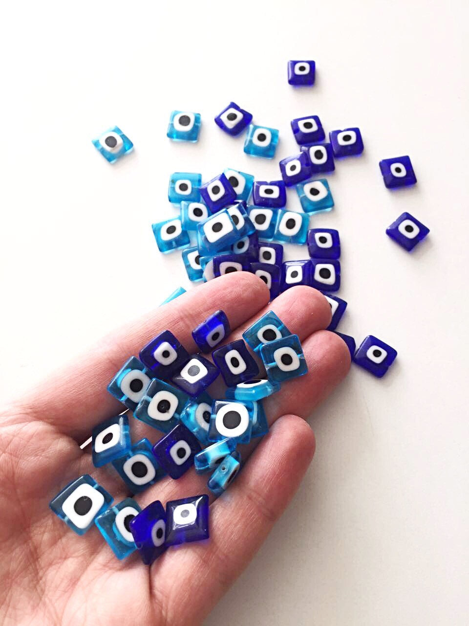 A collection of 10mm flat square glass evil eye beads in turquoise and dark blue, showcasing their unique design and color.