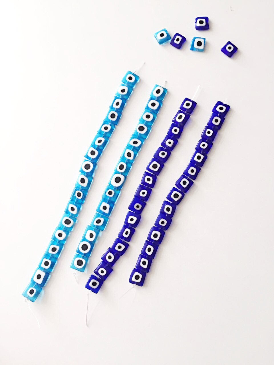 A collection of 10mm flat square glass evil eye beads in turquoise and dark blue, showcasing their unique design and color.