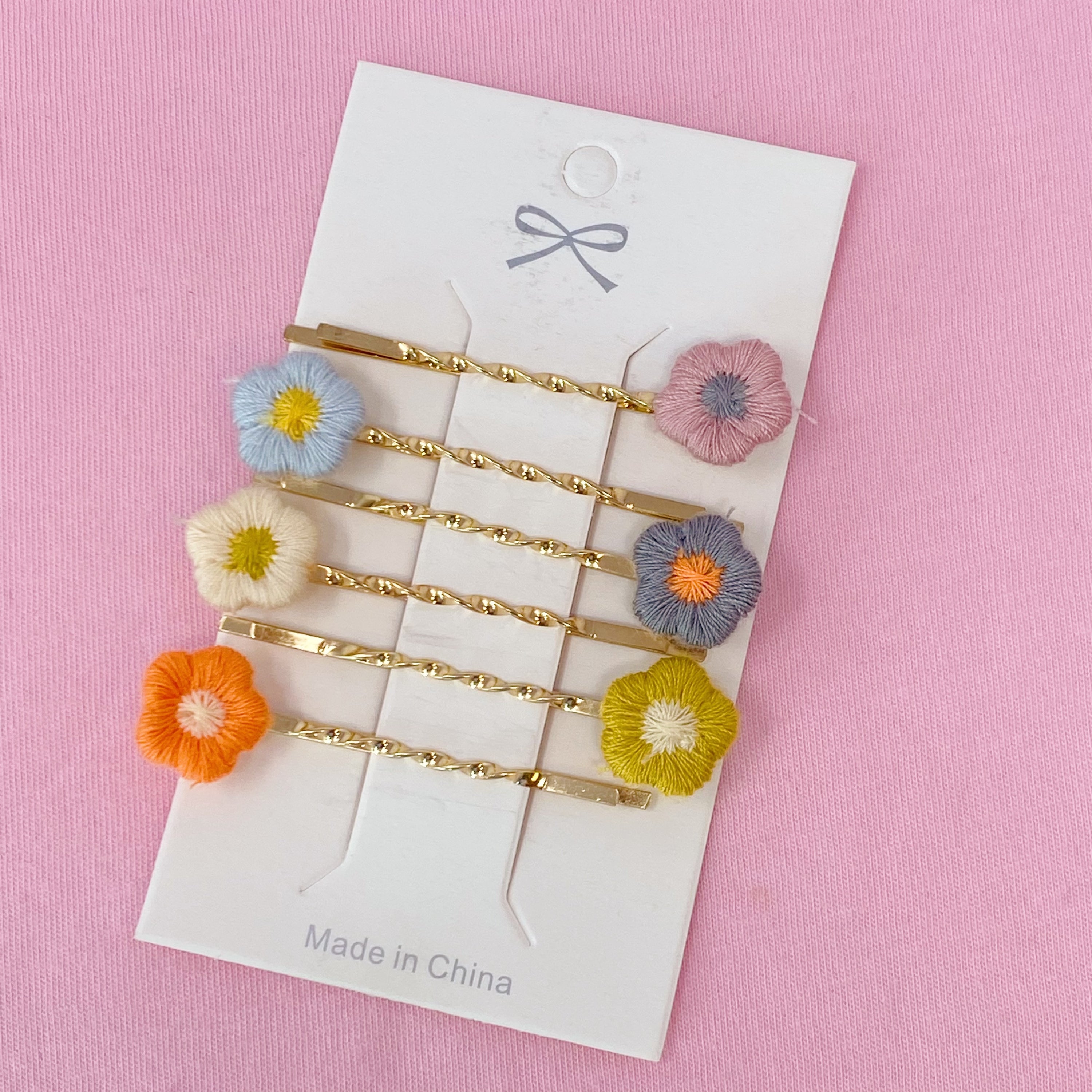 A set of six colorful bobby pins featuring adorable yarn flower designs, beautifully arranged in a clear cello bag.