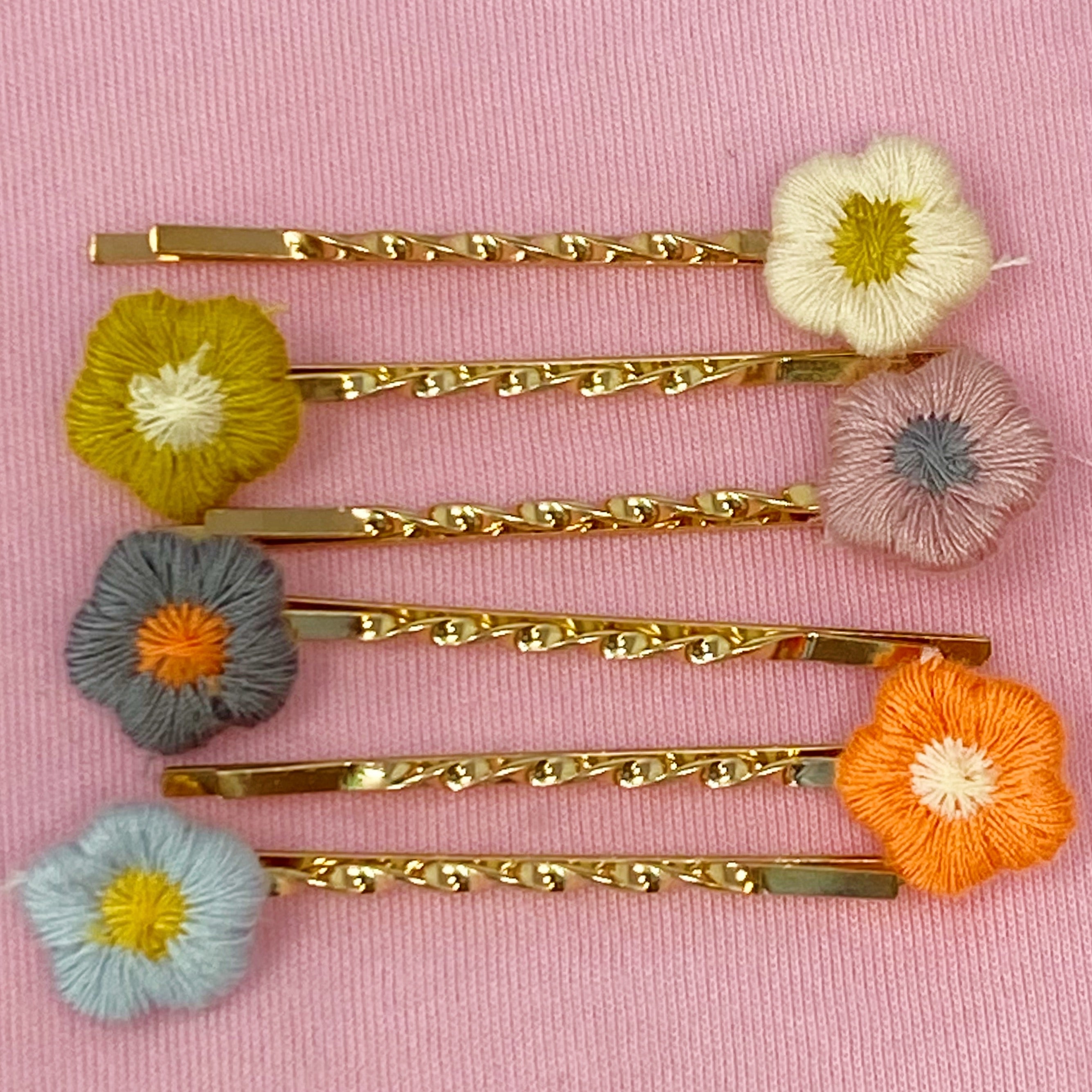 A set of six colorful bobby pins featuring adorable yarn flower designs, beautifully arranged in a clear cello bag.