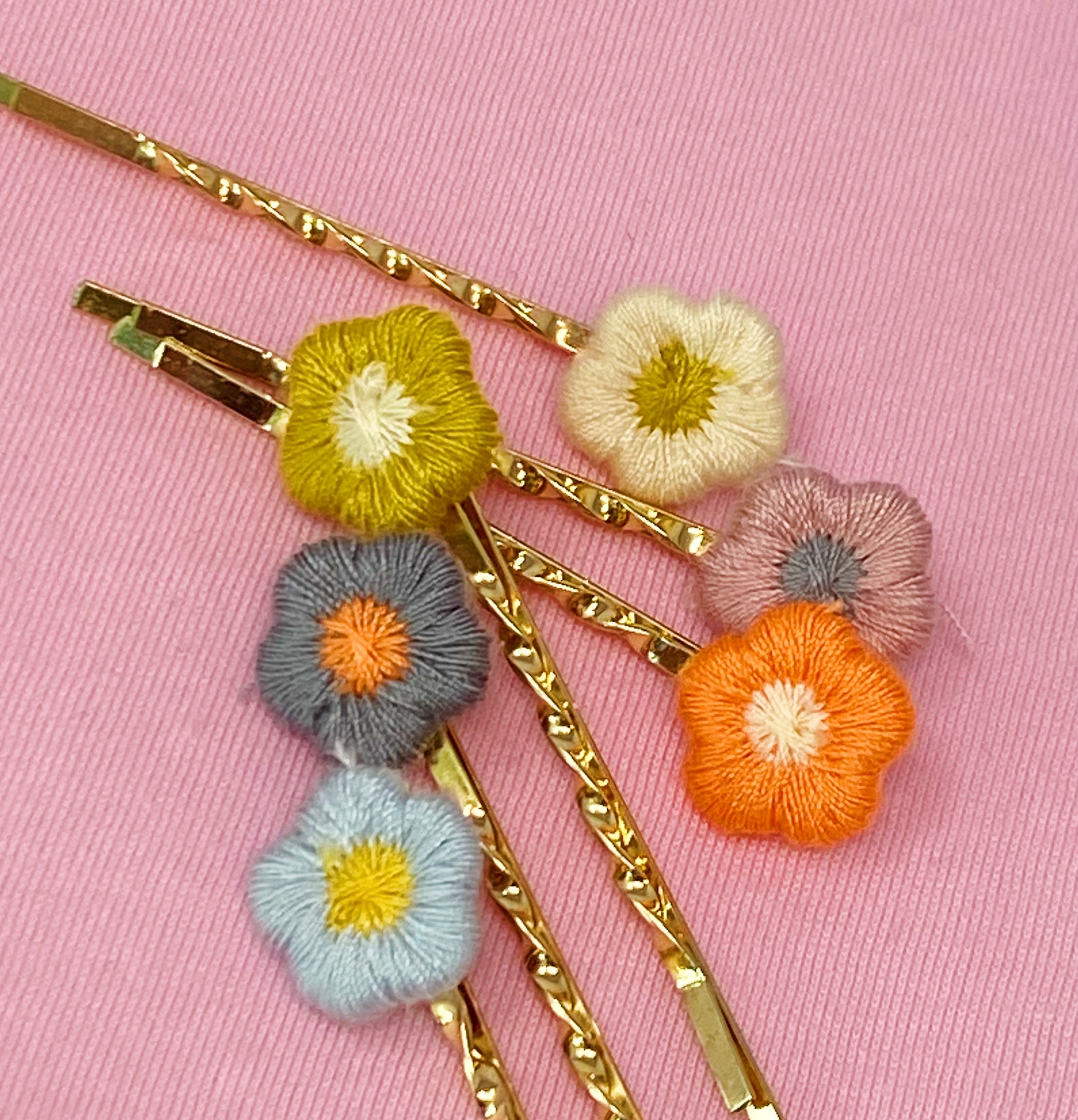 A set of six colorful bobby pins featuring adorable yarn flower designs, beautifully arranged in a clear cello bag.