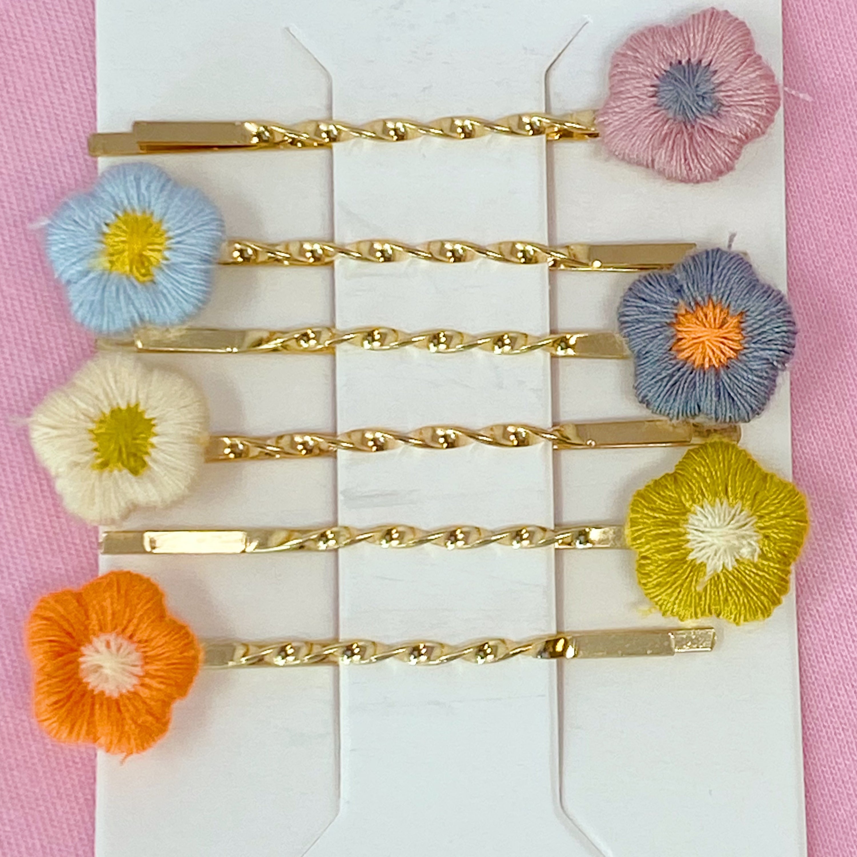 A set of six colorful bobby pins featuring adorable yarn flower designs, beautifully arranged in a clear cello bag.