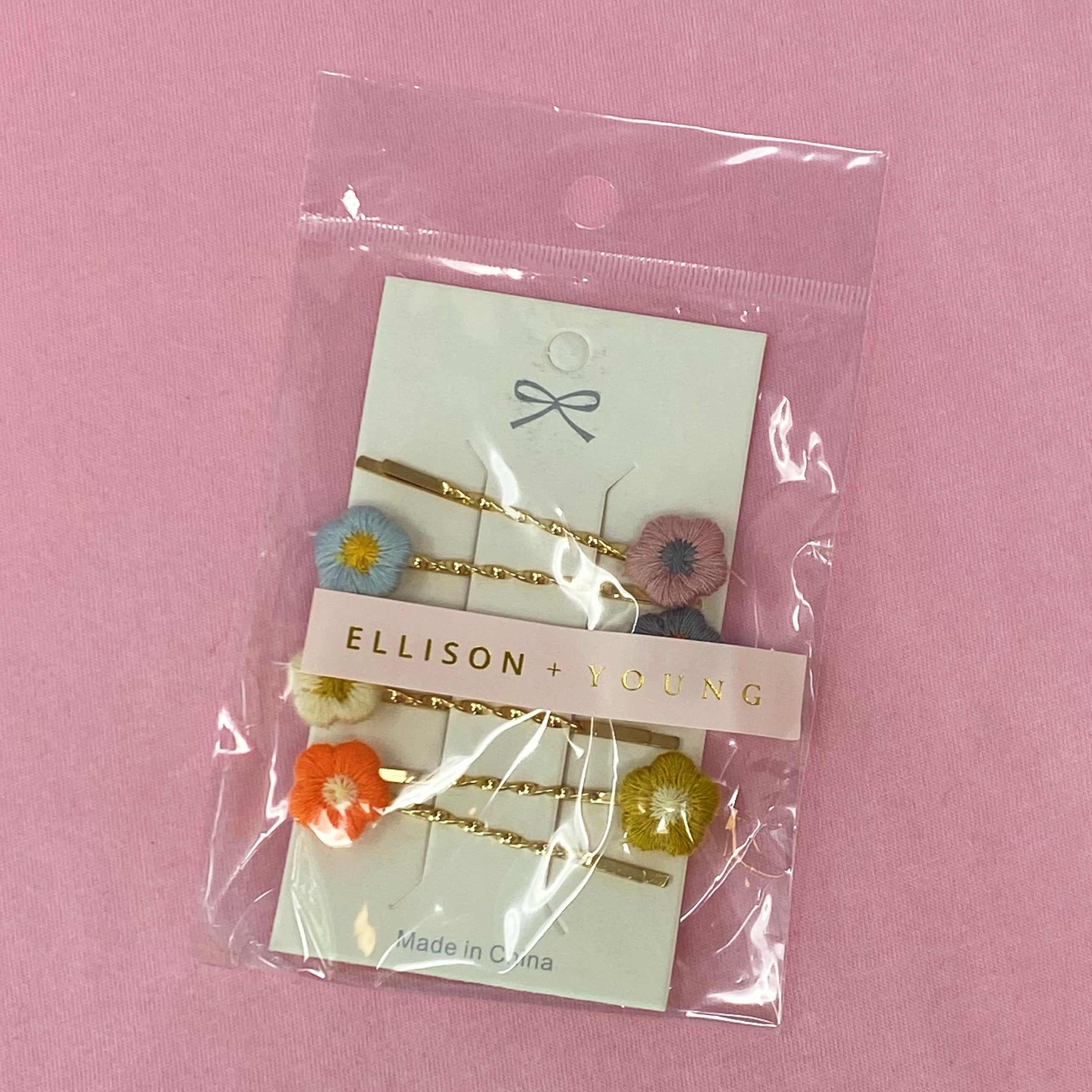 A set of six colorful bobby pins featuring adorable yarn flower designs, beautifully arranged in a clear cello bag.