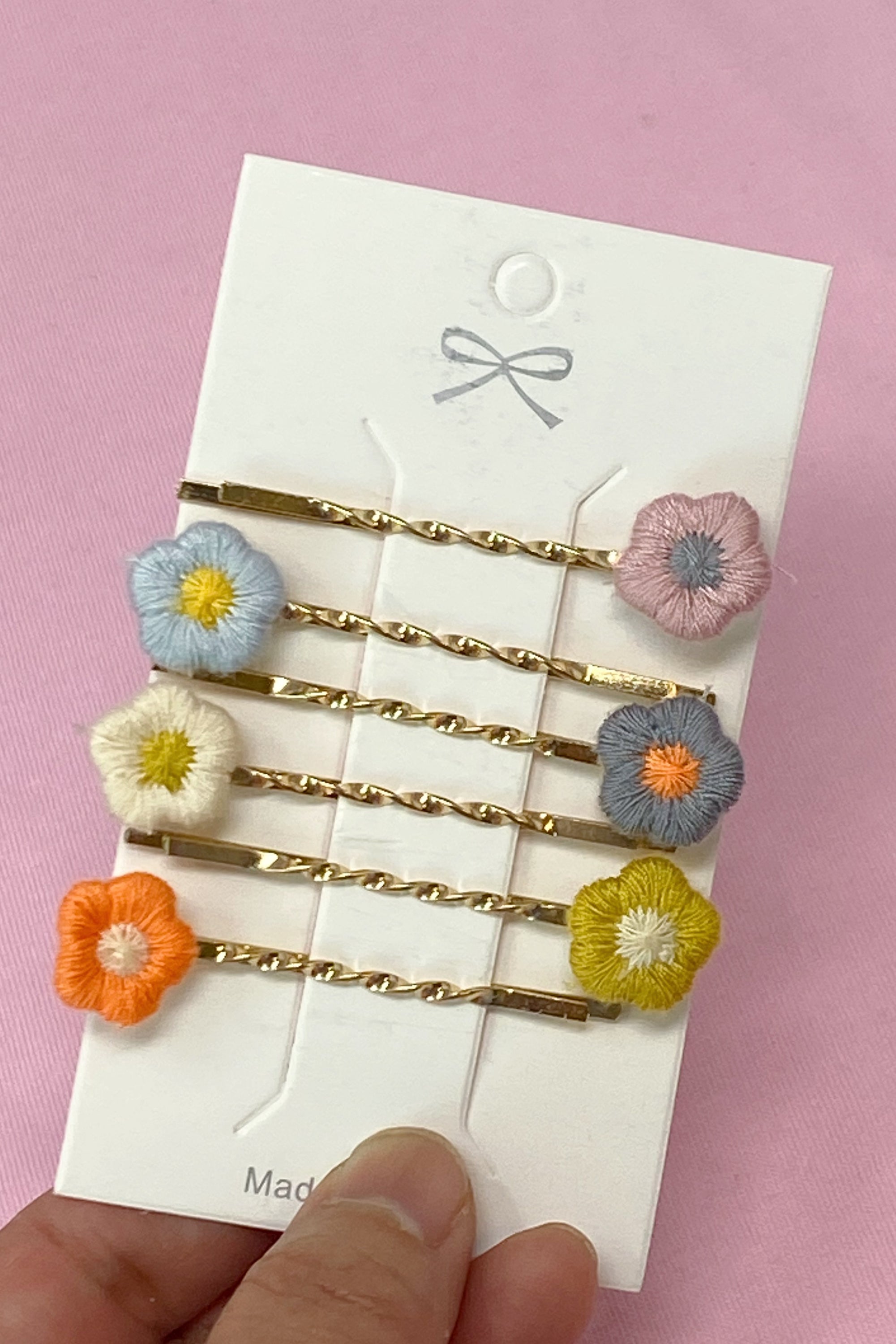 A set of six colorful bobby pins featuring adorable yarn flower designs, beautifully arranged in a clear cello bag.