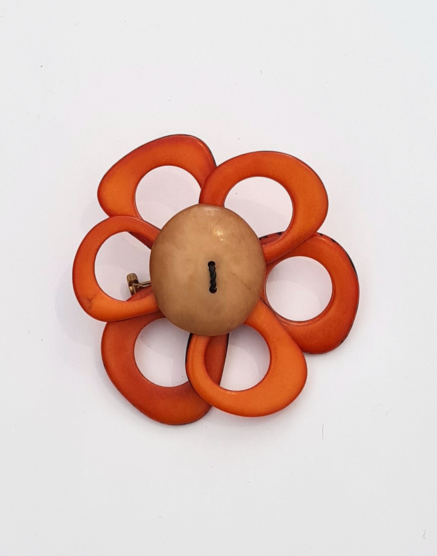 A delicate flower brooch designed as a daisy, made from slices of tagua, showcasing natural variations in color and texture.