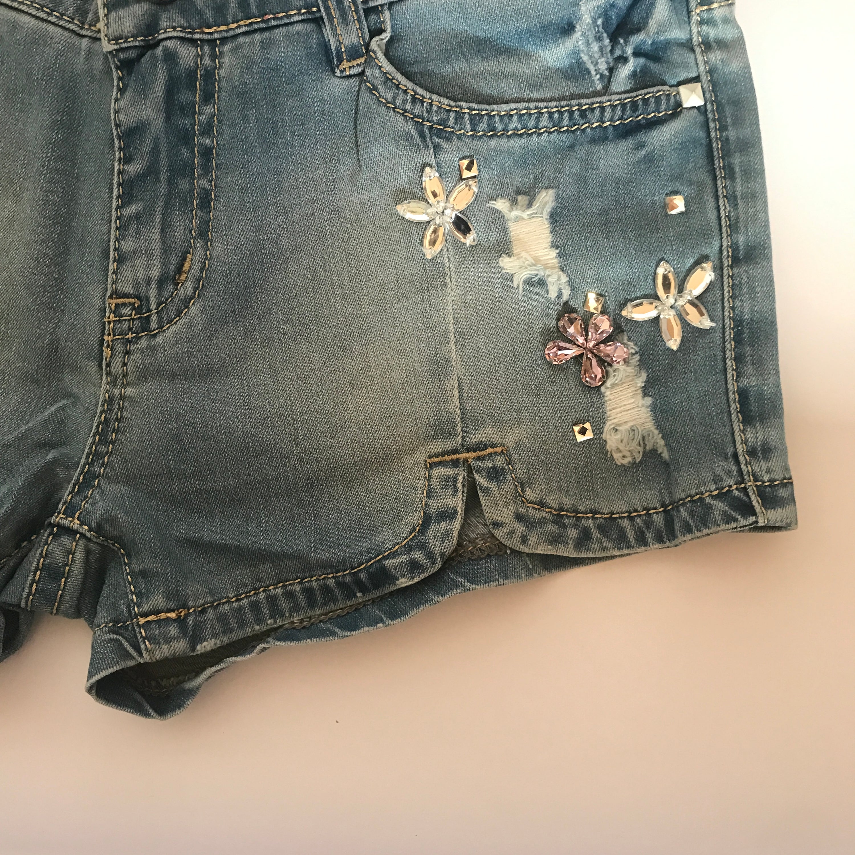 A pair of stylish denim shorts adorned with flower rhinestones, showcasing a trendy summer look.