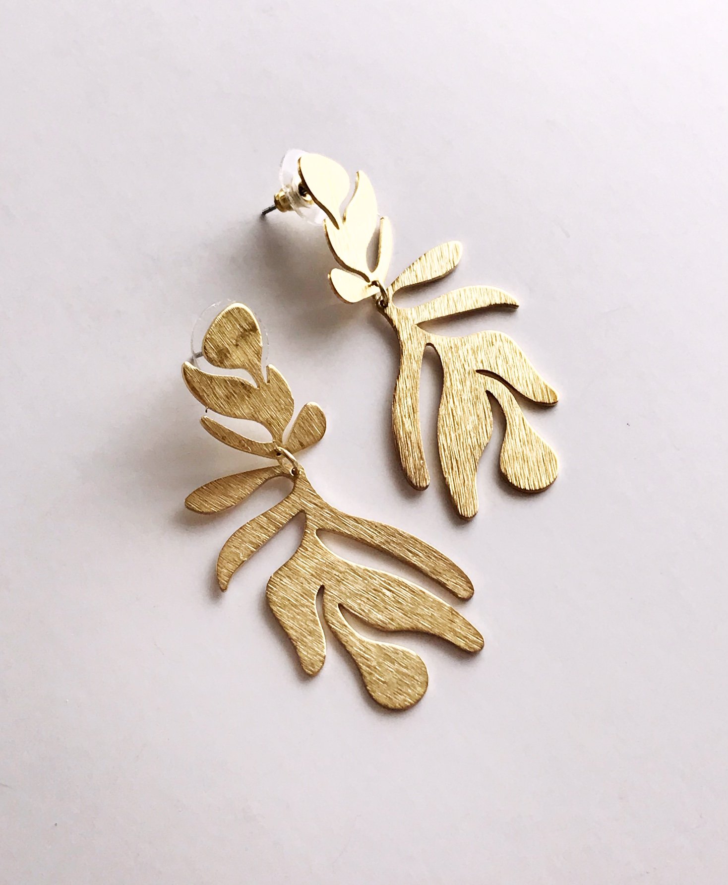 A pair of lightweight floral-inspired frond earrings in brushed brass, showcasing their elegant design and stainless steel ear posts.