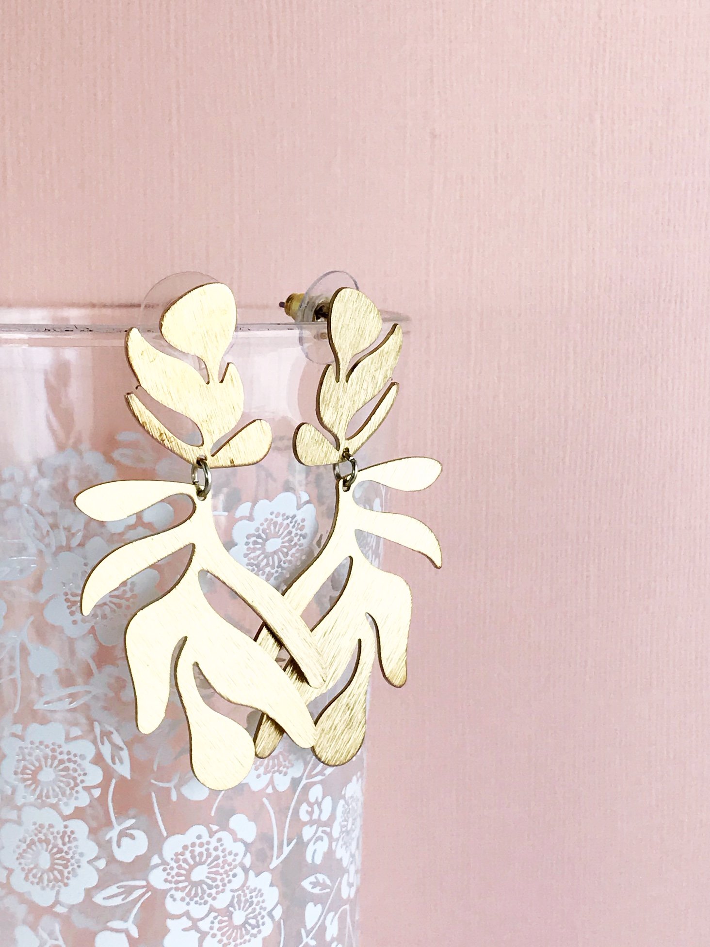 A pair of lightweight floral-inspired frond earrings in brushed brass, showcasing their elegant design and stainless steel ear posts.