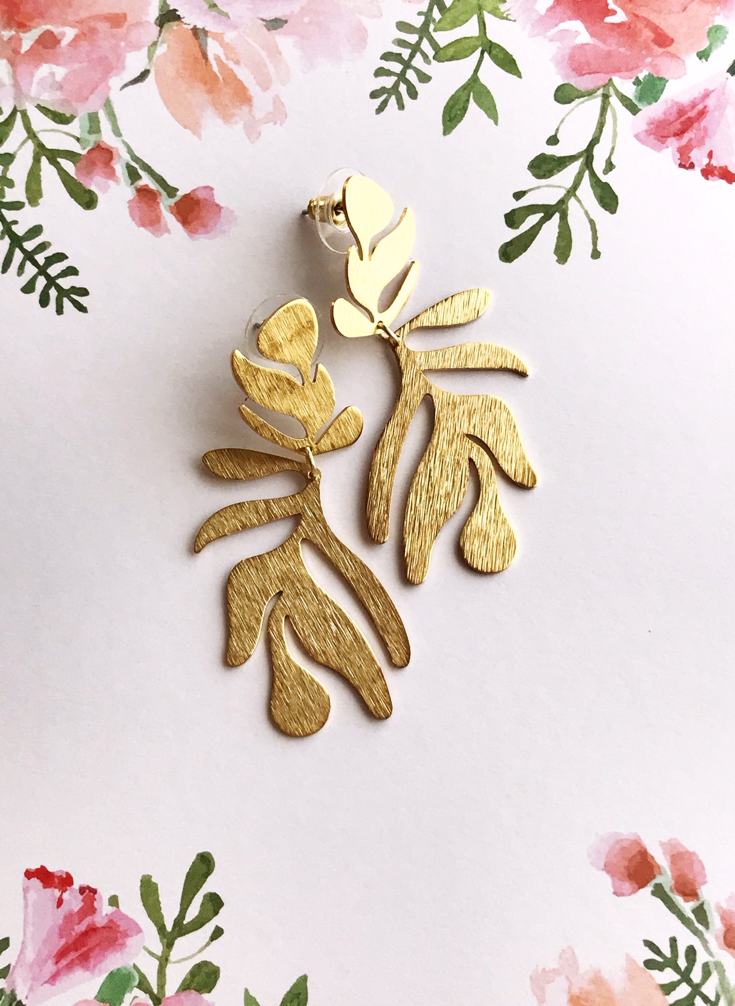 A pair of lightweight floral-inspired frond earrings in brushed brass, showcasing their elegant design and stainless steel ear posts.