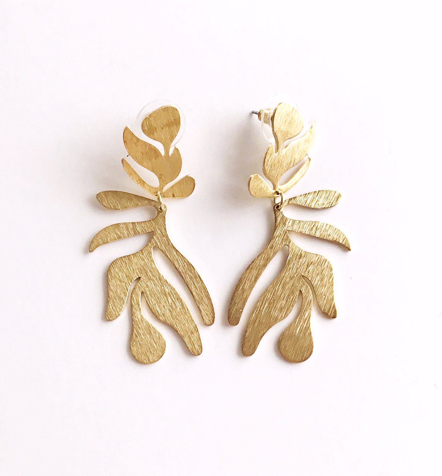 A pair of lightweight floral-inspired frond earrings in brushed brass, showcasing their elegant design and stainless steel ear posts.