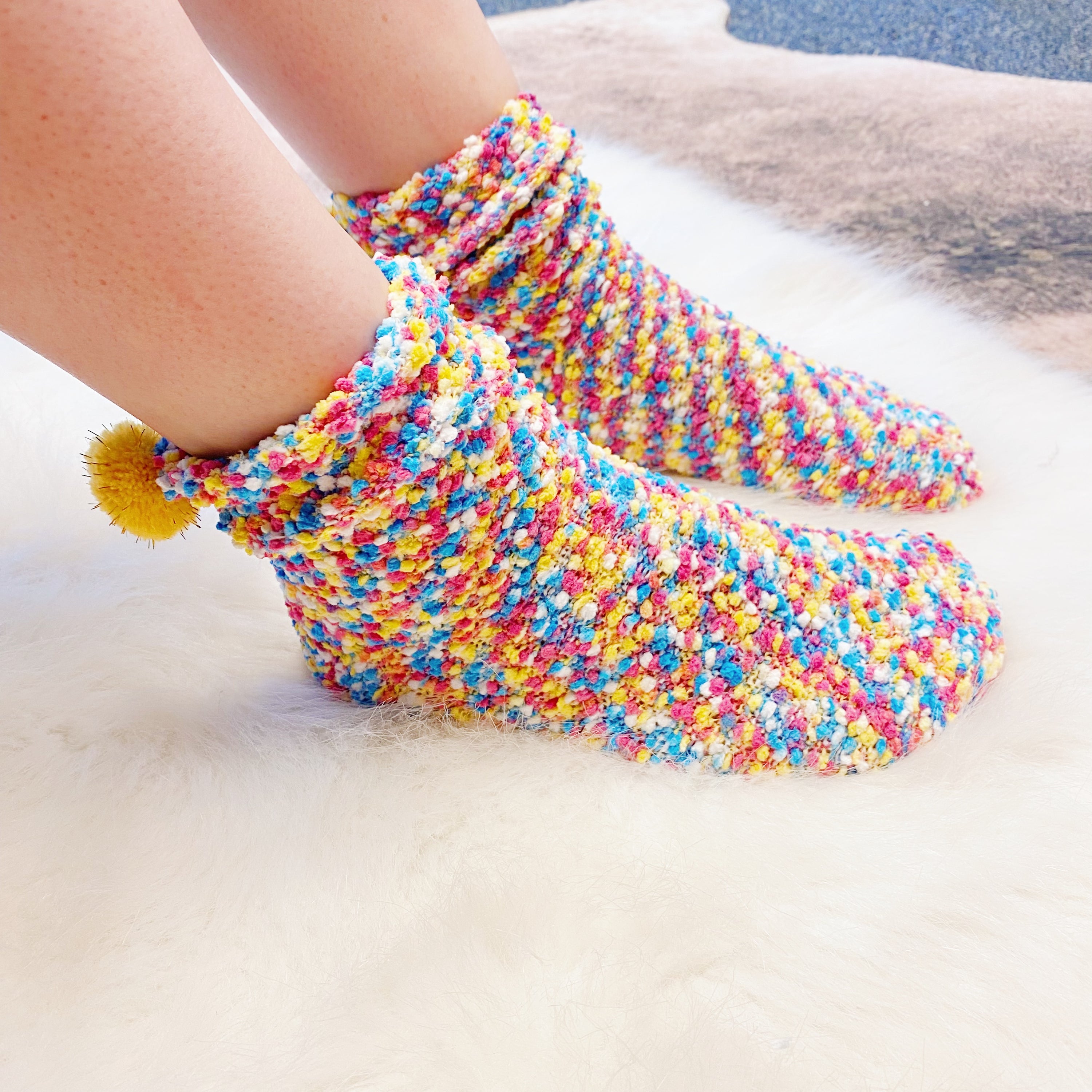 Soft and fuzzy Fuzzy Pom Confetti Socks with a cute pom detail on the back, displayed in cupcake packaging.