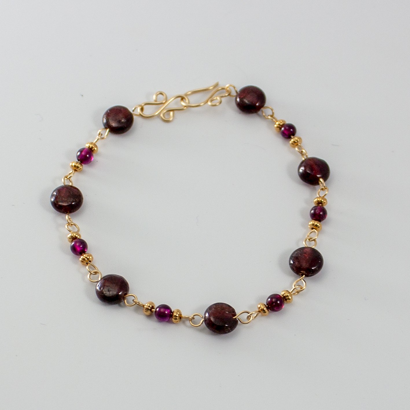 Garnet 14k Gold Filled Chain Bracelet featuring garnet gemstones and gold accents, elegantly displayed on a soft surface.