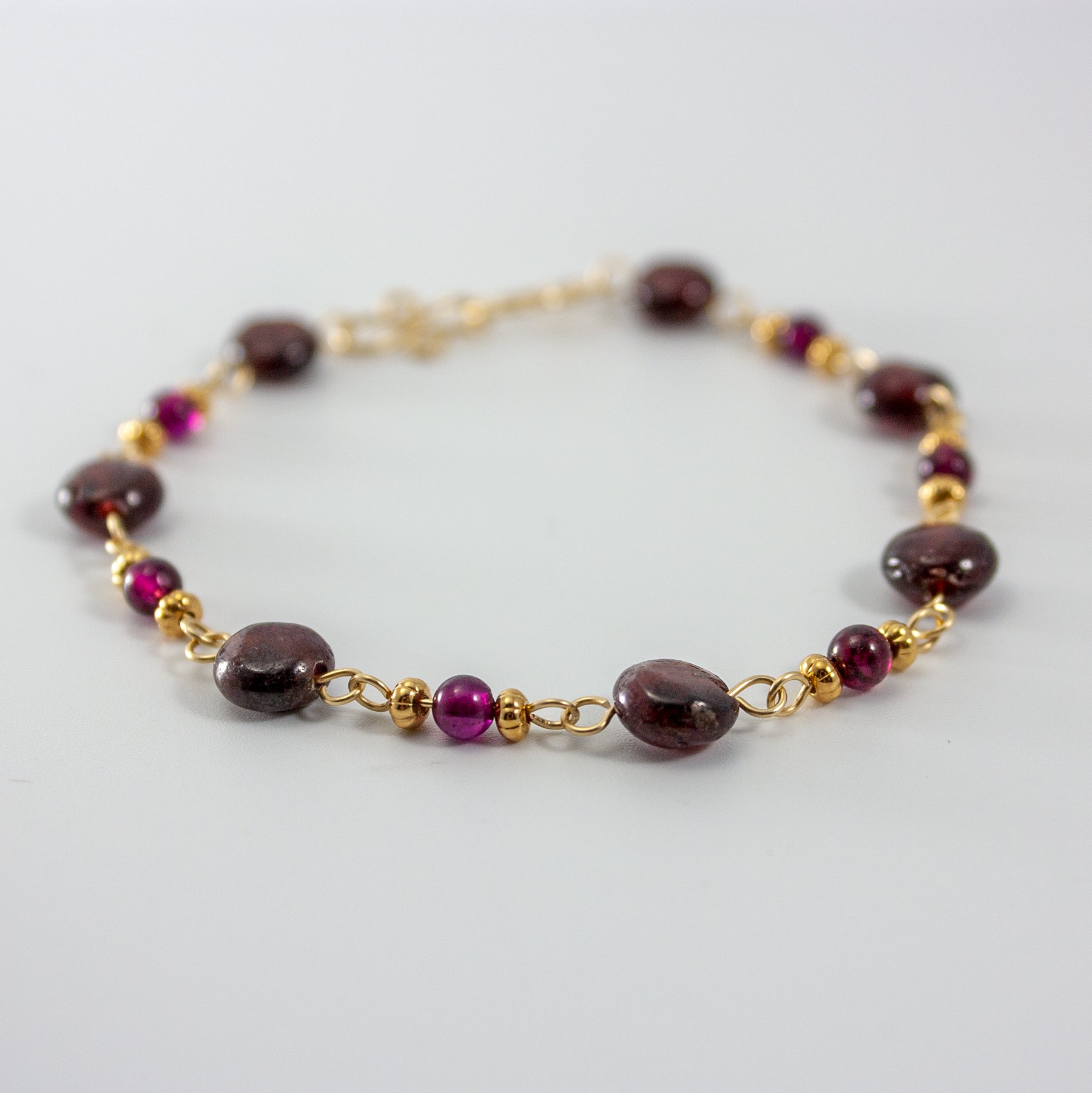 Garnet 14k Gold Filled Chain Bracelet featuring garnet gemstones and gold accents, elegantly displayed on a soft surface.