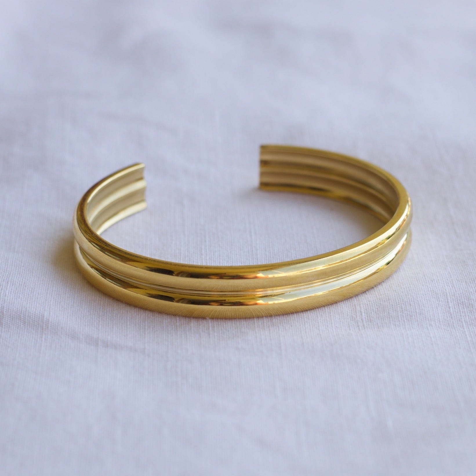 Gil Wide Polished Cuff Bracelet in Gold, showcasing its shiny stainless steel and 18K gold plating with an adjustable open cuff design.