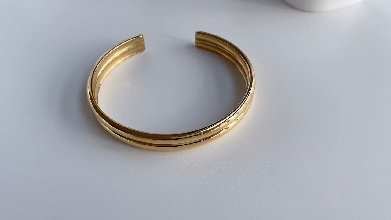 Gil Wide Polished Cuff Bracelet in Gold, showcasing its shiny stainless steel and 18K gold plating with an adjustable open cuff design.