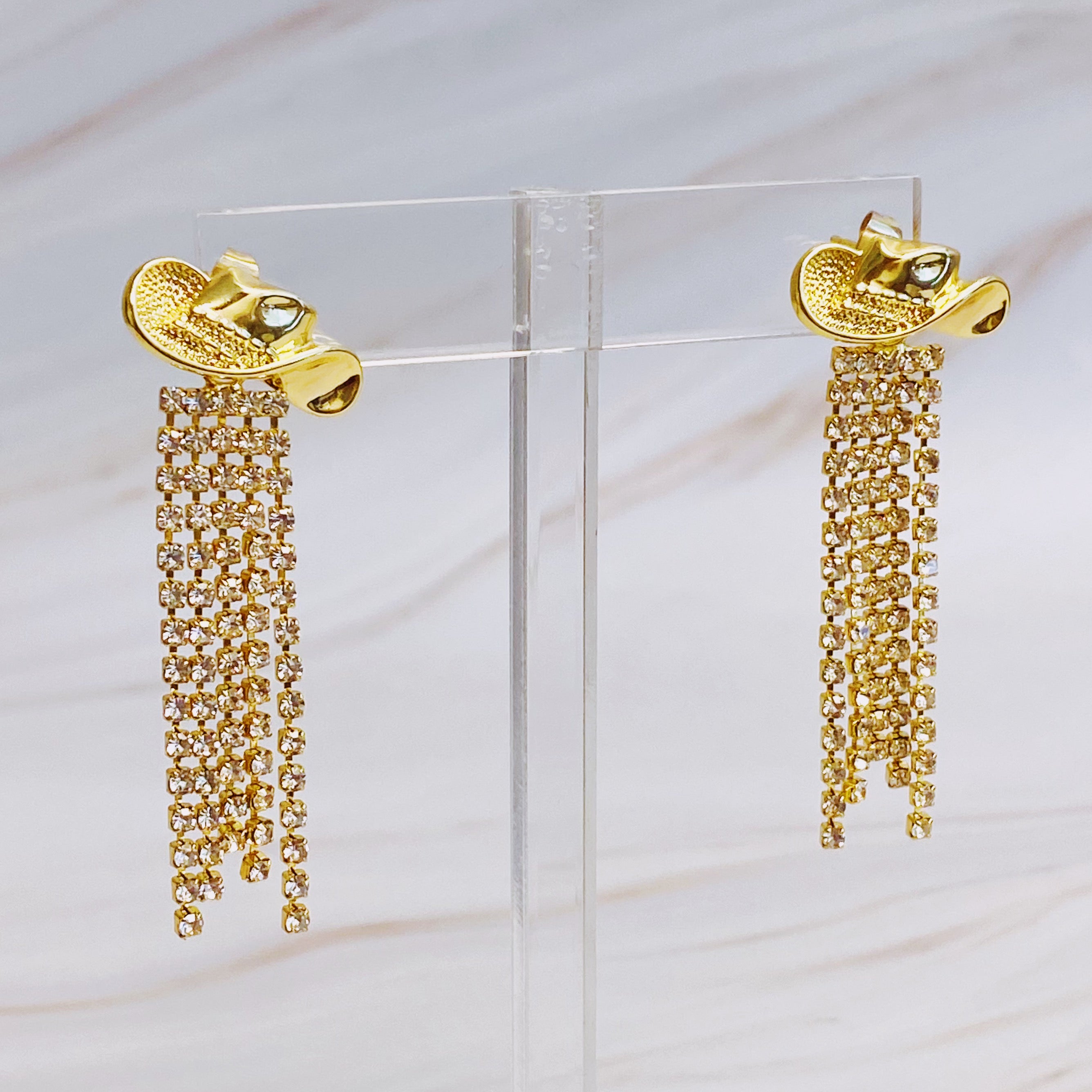 A pair of sparkly gold plated brass cowgirl earrings with a 2-inch drop, showcasing a glamorous design.