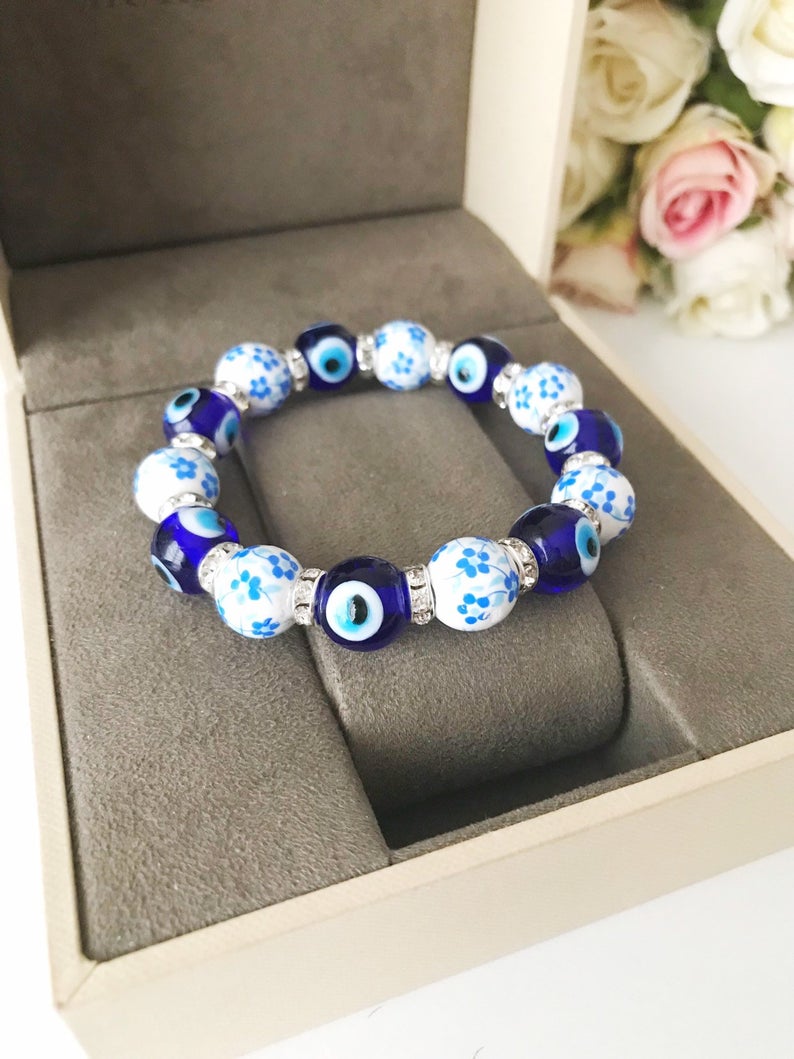 A beautiful Glass Evil Eye Bracelet featuring ceramic and blue glass beads, showcasing a vibrant blue evil eye charm.