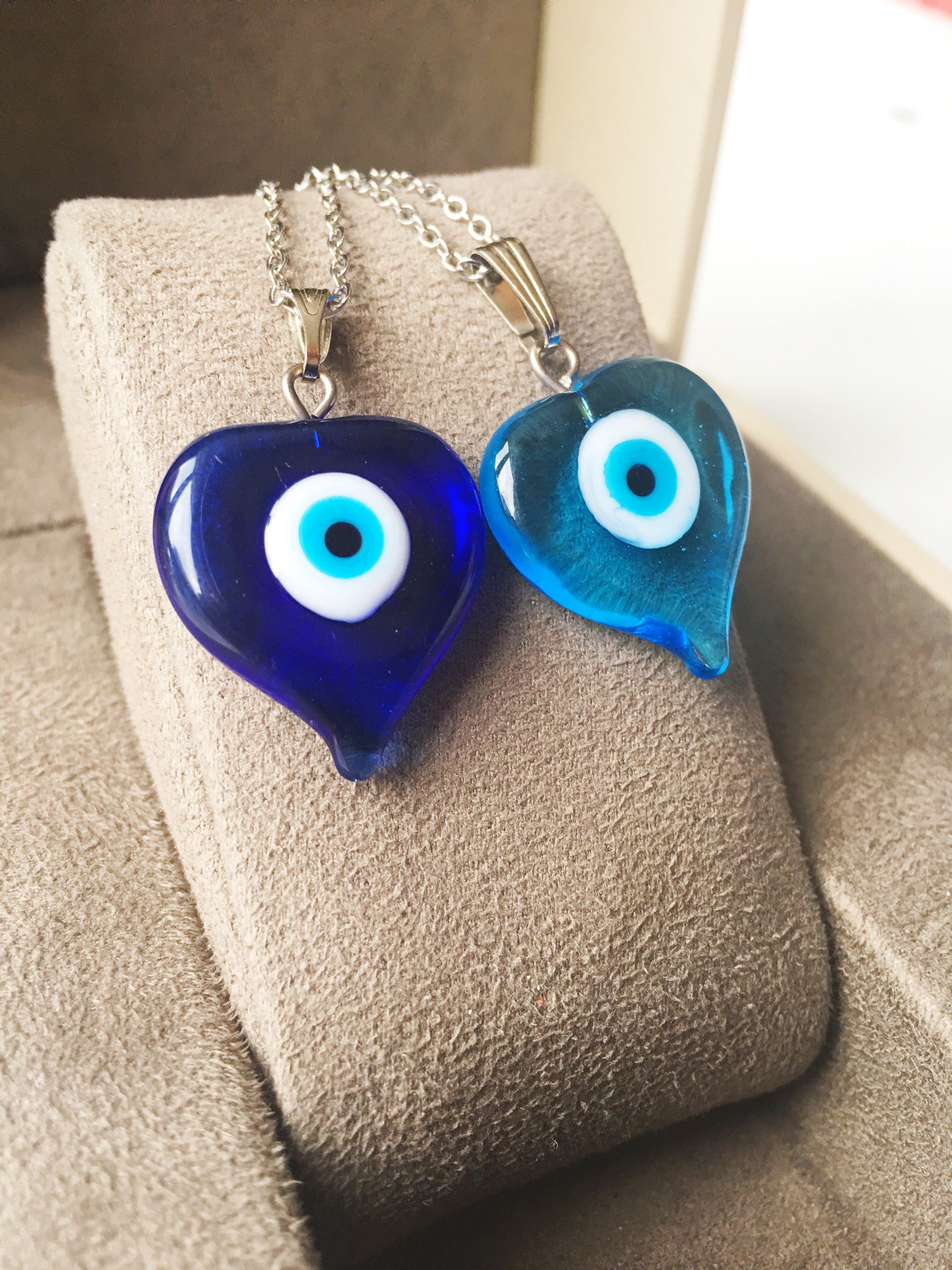 A beautiful Glass Evil Eye Necklace featuring a blue evil eye bead on a stainless steel chain, available in round, heart, and oval shapes.