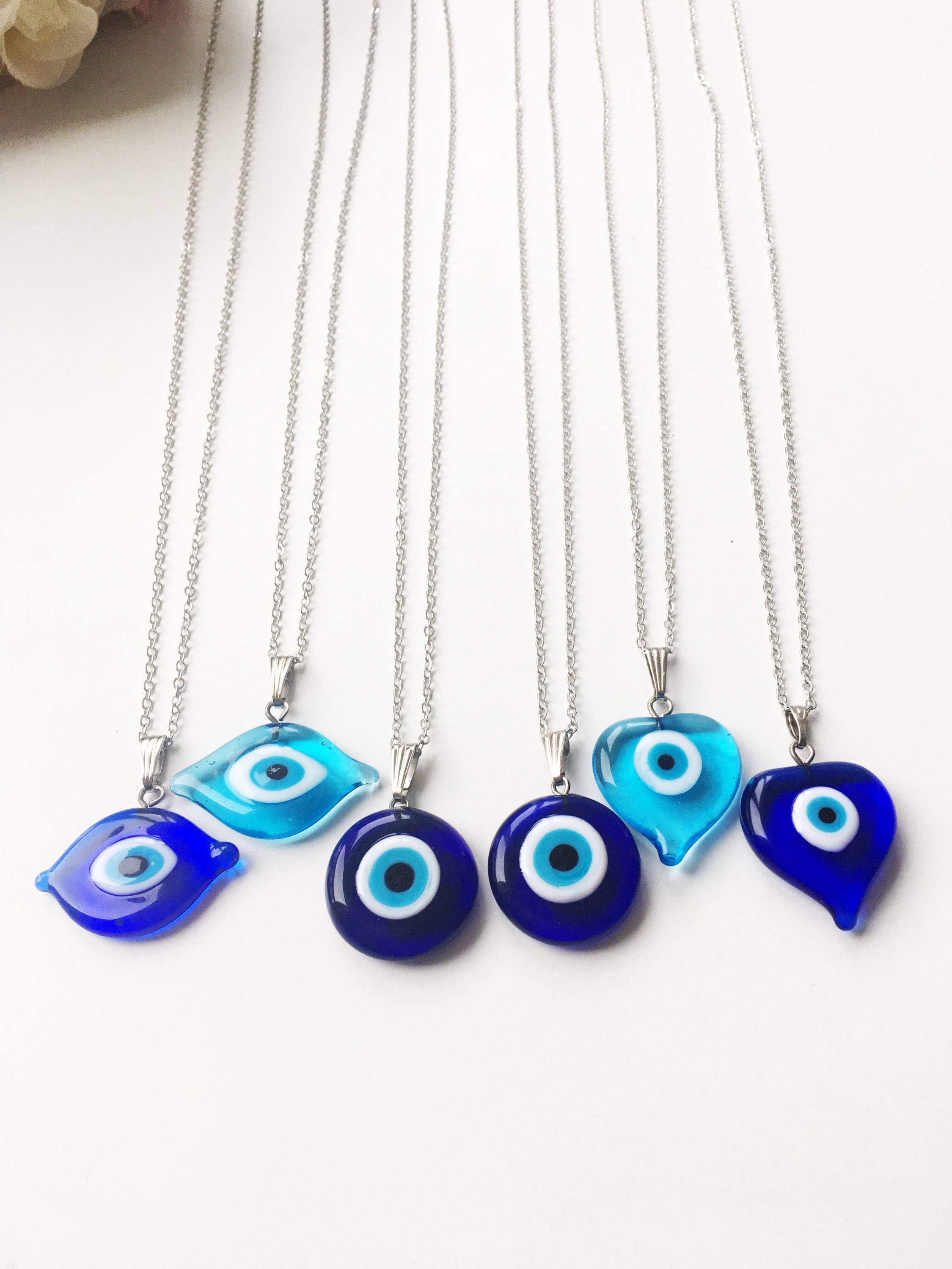 A beautiful Glass Evil Eye Necklace featuring a blue evil eye bead on a stainless steel chain, available in round, heart, and oval shapes.