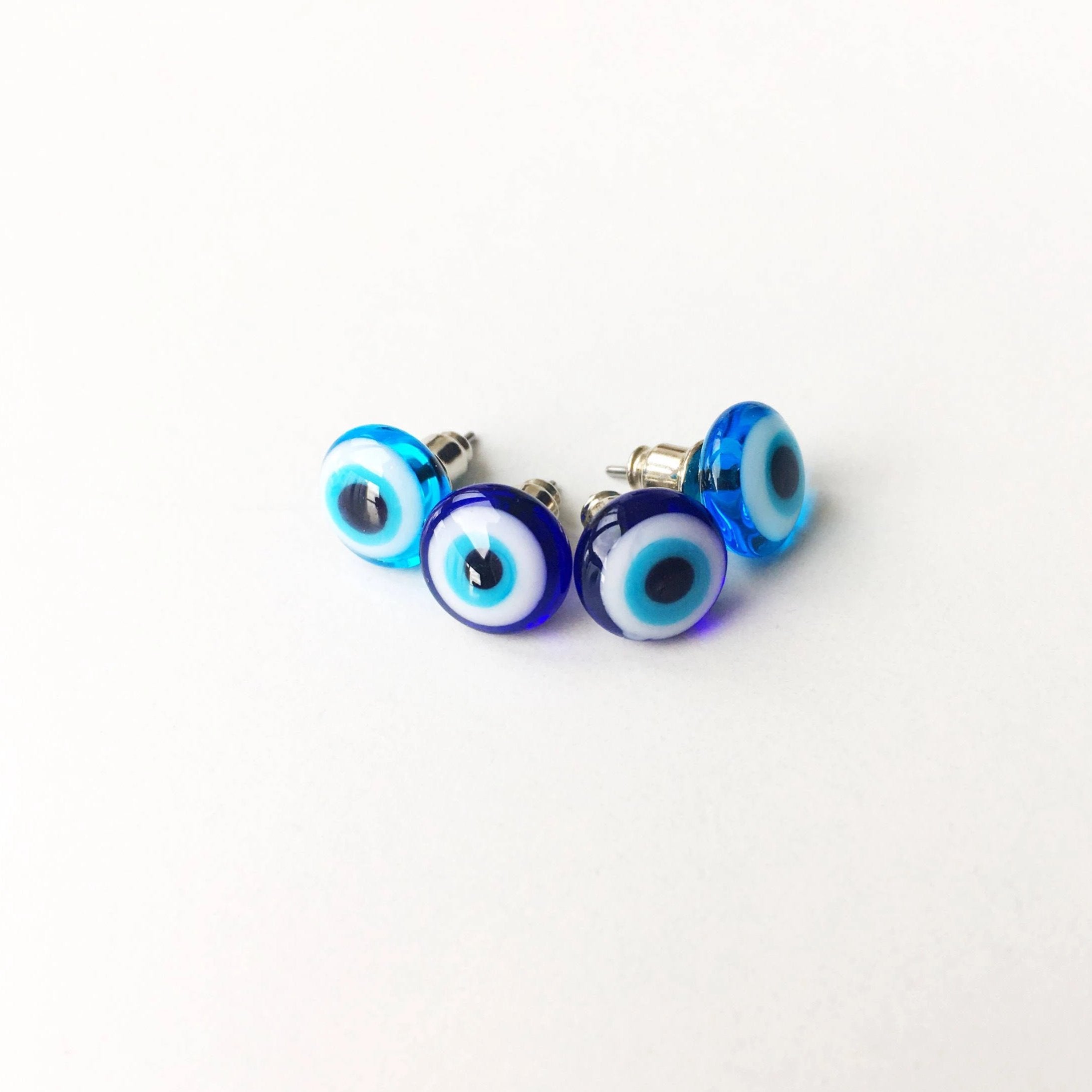 A pair of handmade glass evil eye stud earrings in dark blue and turquoise, featuring a protective eye design set in stainless steel.