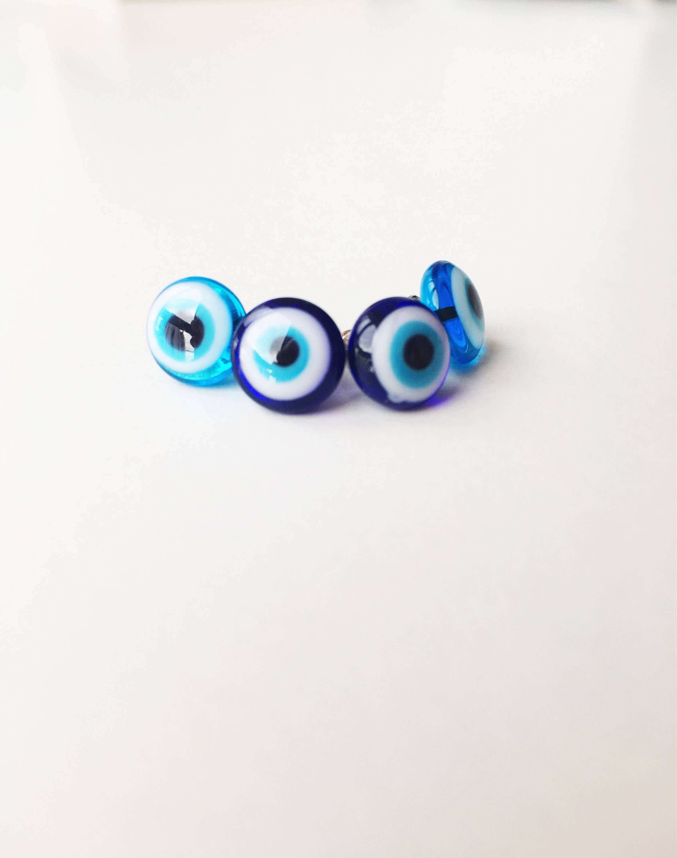 A pair of handmade glass evil eye stud earrings in dark blue and turquoise, featuring a protective eye design set in stainless steel.