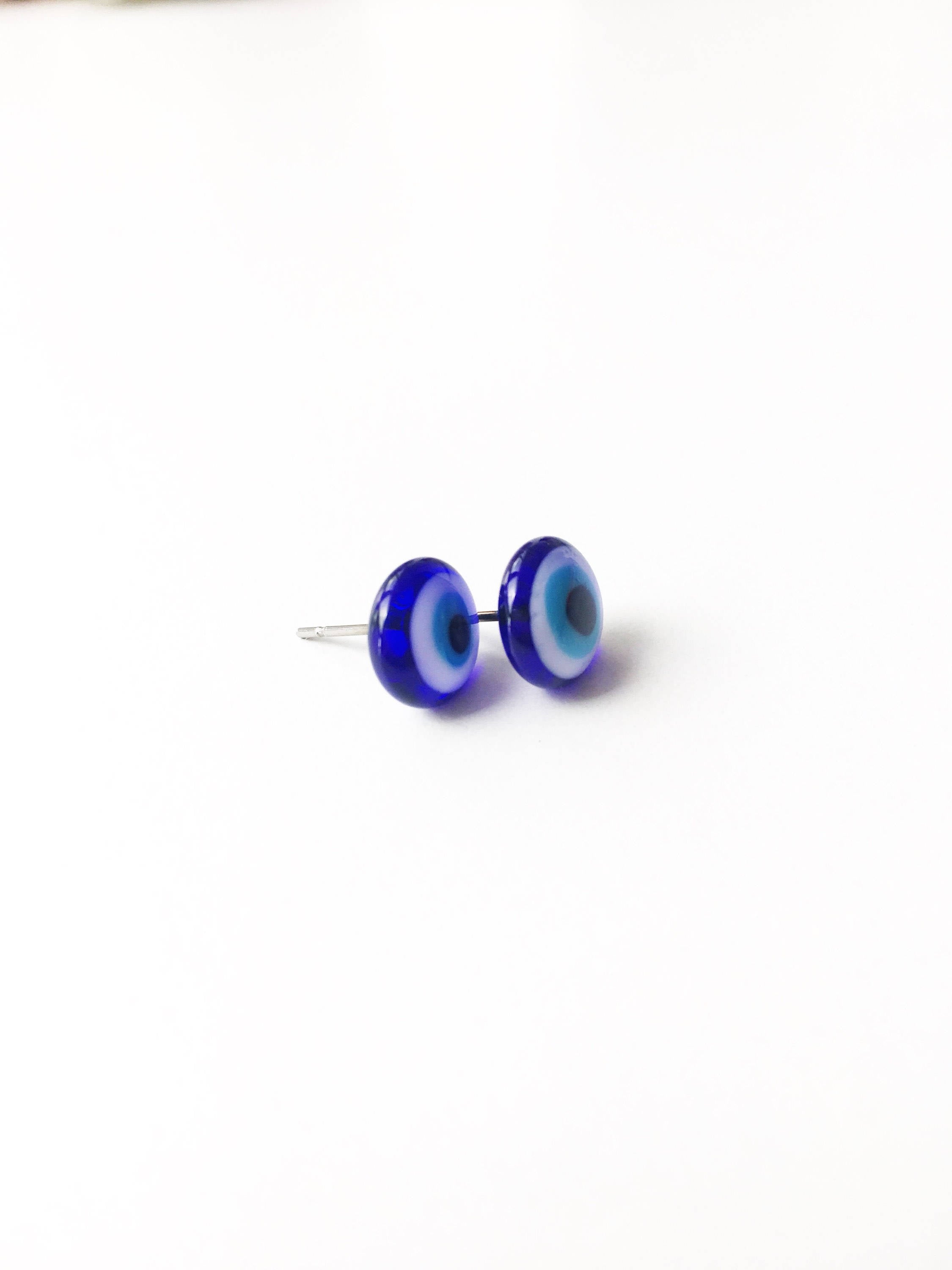 A pair of handmade glass evil eye stud earrings in dark blue and turquoise, featuring a protective eye design set in stainless steel.