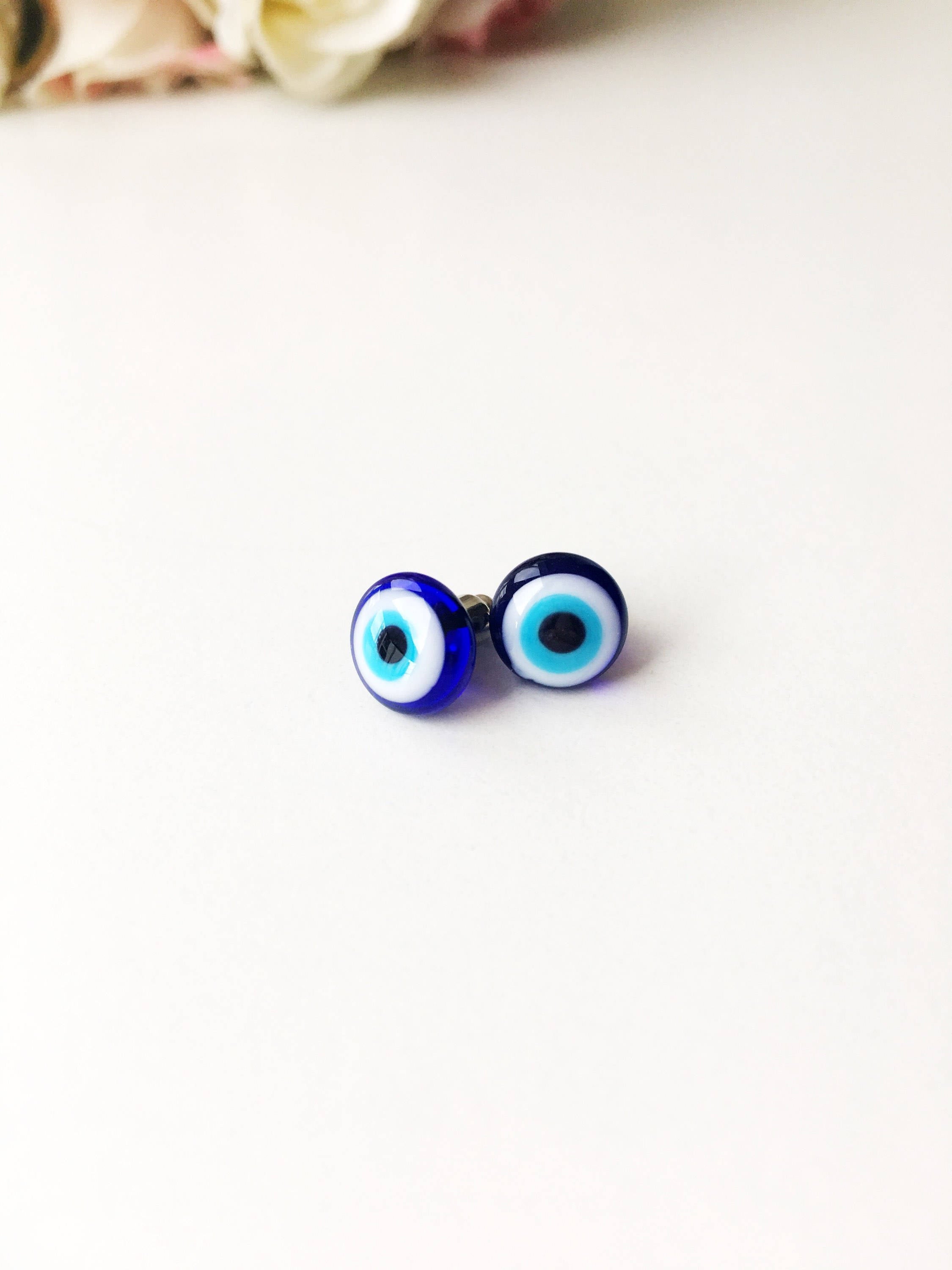 A pair of handmade glass evil eye stud earrings in dark blue and turquoise, featuring a protective eye design set in stainless steel.