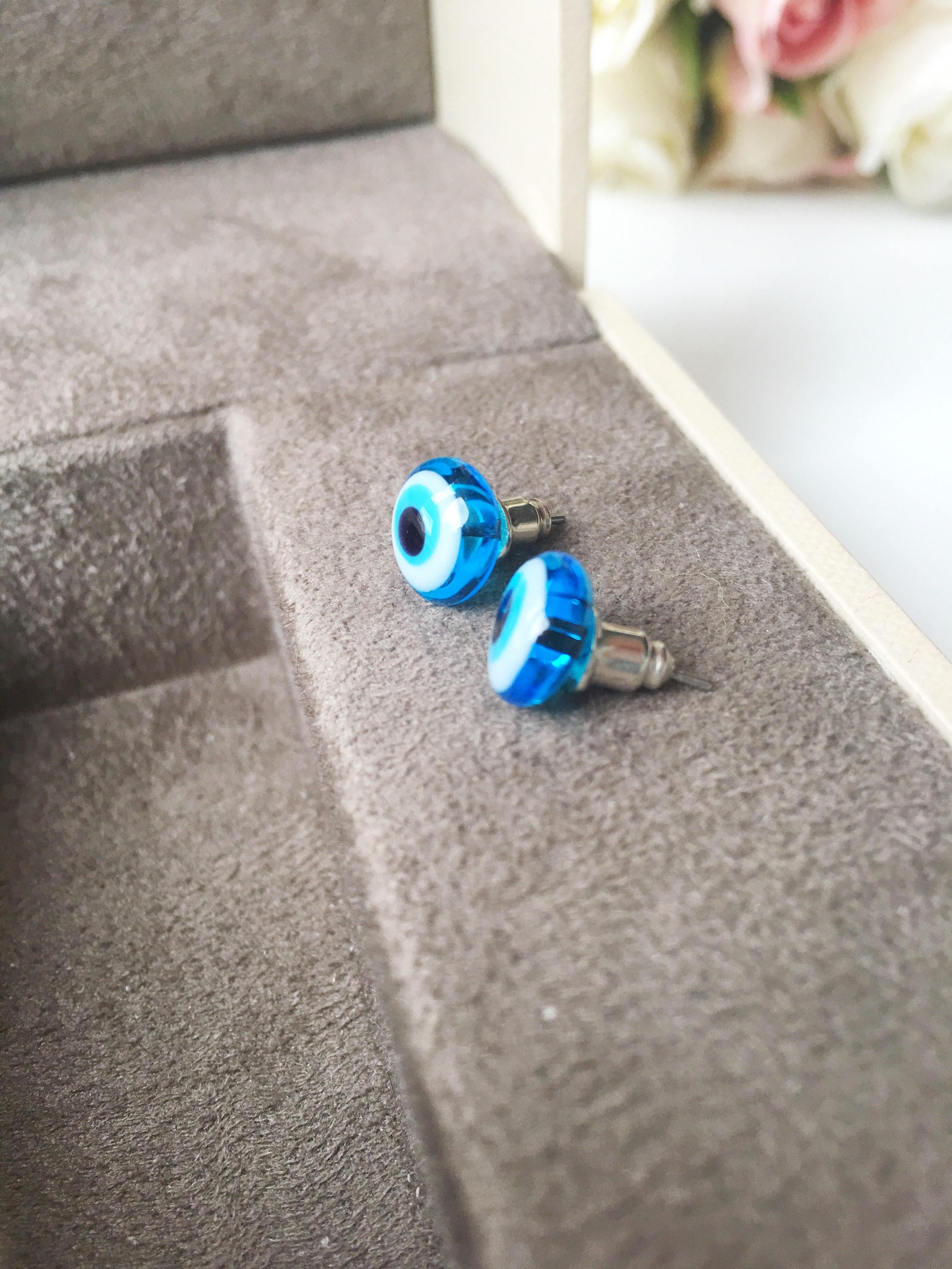 A pair of handmade glass evil eye stud earrings in dark blue and turquoise, featuring a protective eye design set in stainless steel.