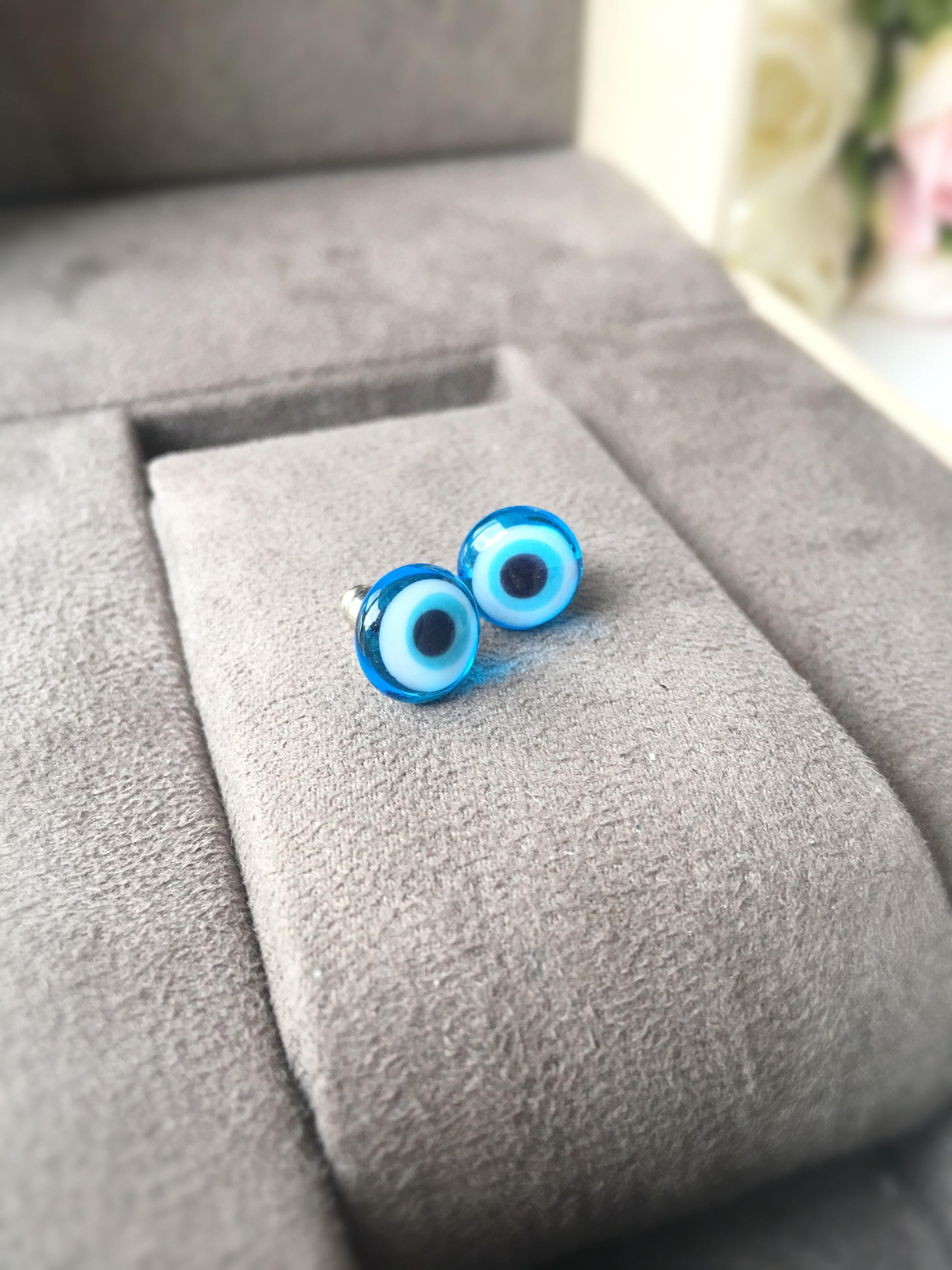 A pair of handmade glass evil eye stud earrings in dark blue and turquoise, featuring a protective eye design set in stainless steel.