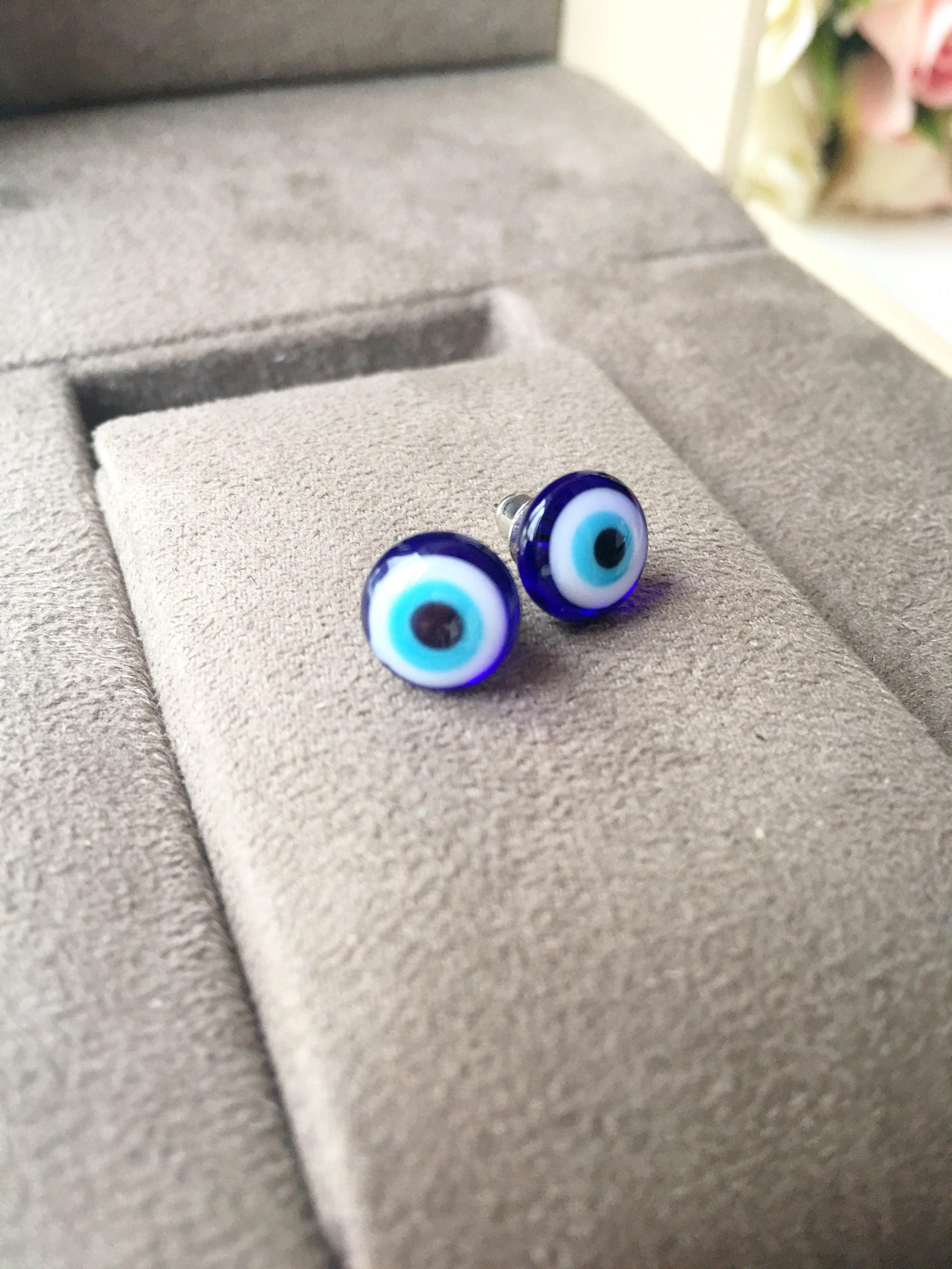 A pair of handmade glass evil eye stud earrings in dark blue and turquoise, featuring a protective eye design set in stainless steel.