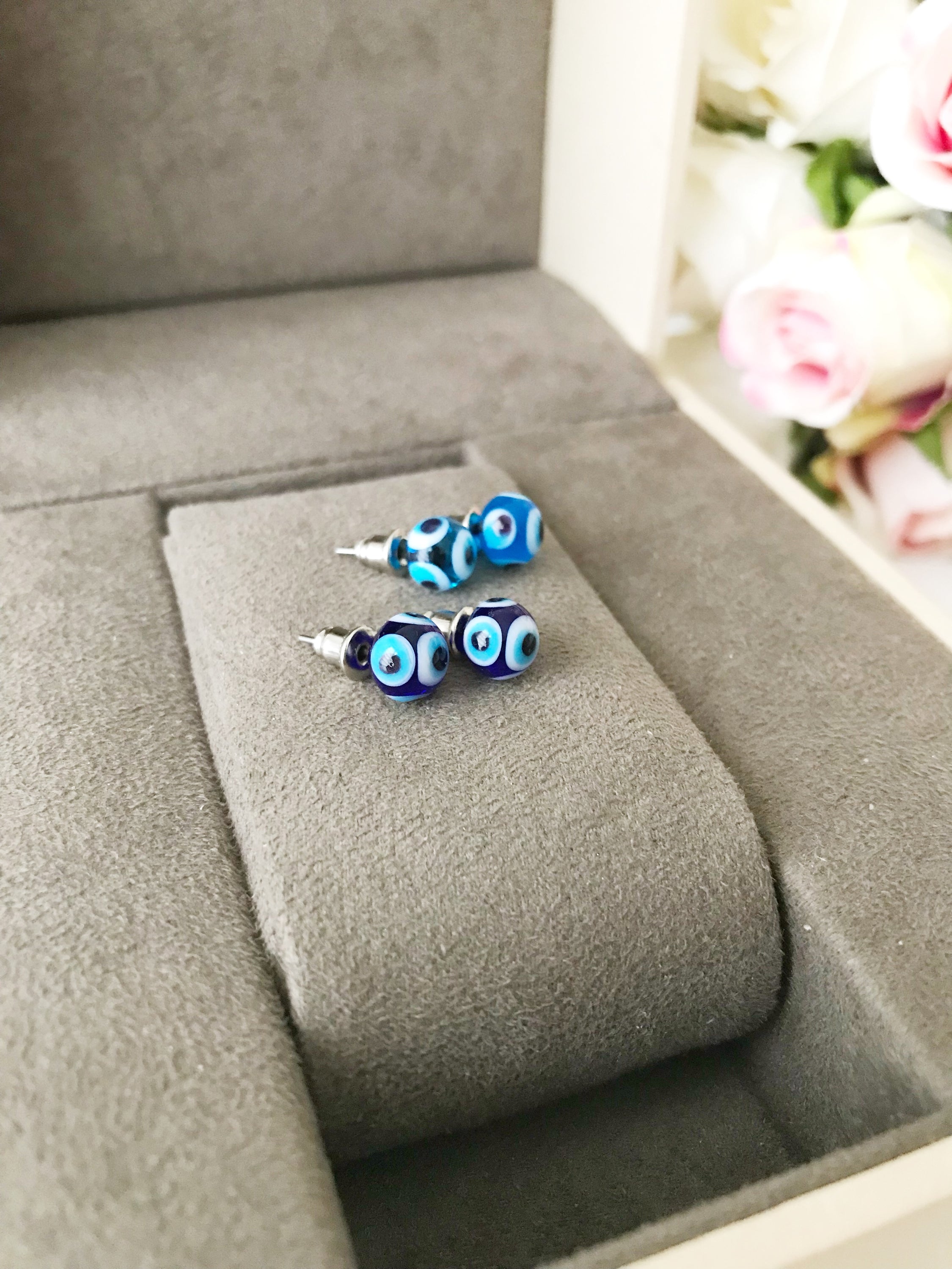 A pair of handmade glass evil eye stud earrings in dark blue and turquoise, symbolizing protection and good luck, displayed elegantly.