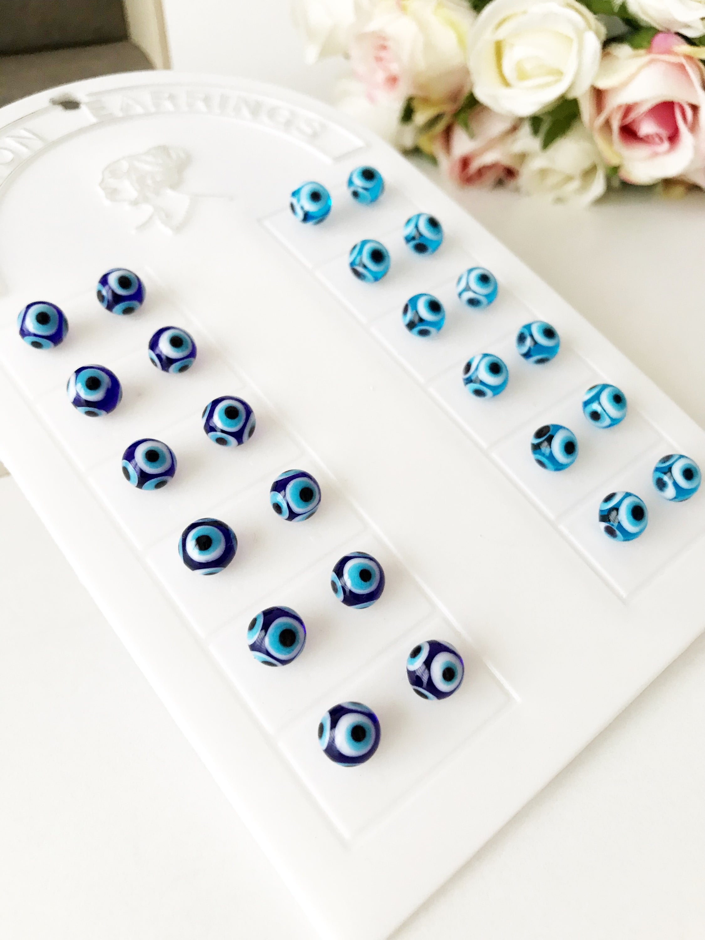 A pair of handmade glass evil eye stud earrings in dark blue and turquoise, symbolizing protection and good luck, displayed elegantly.