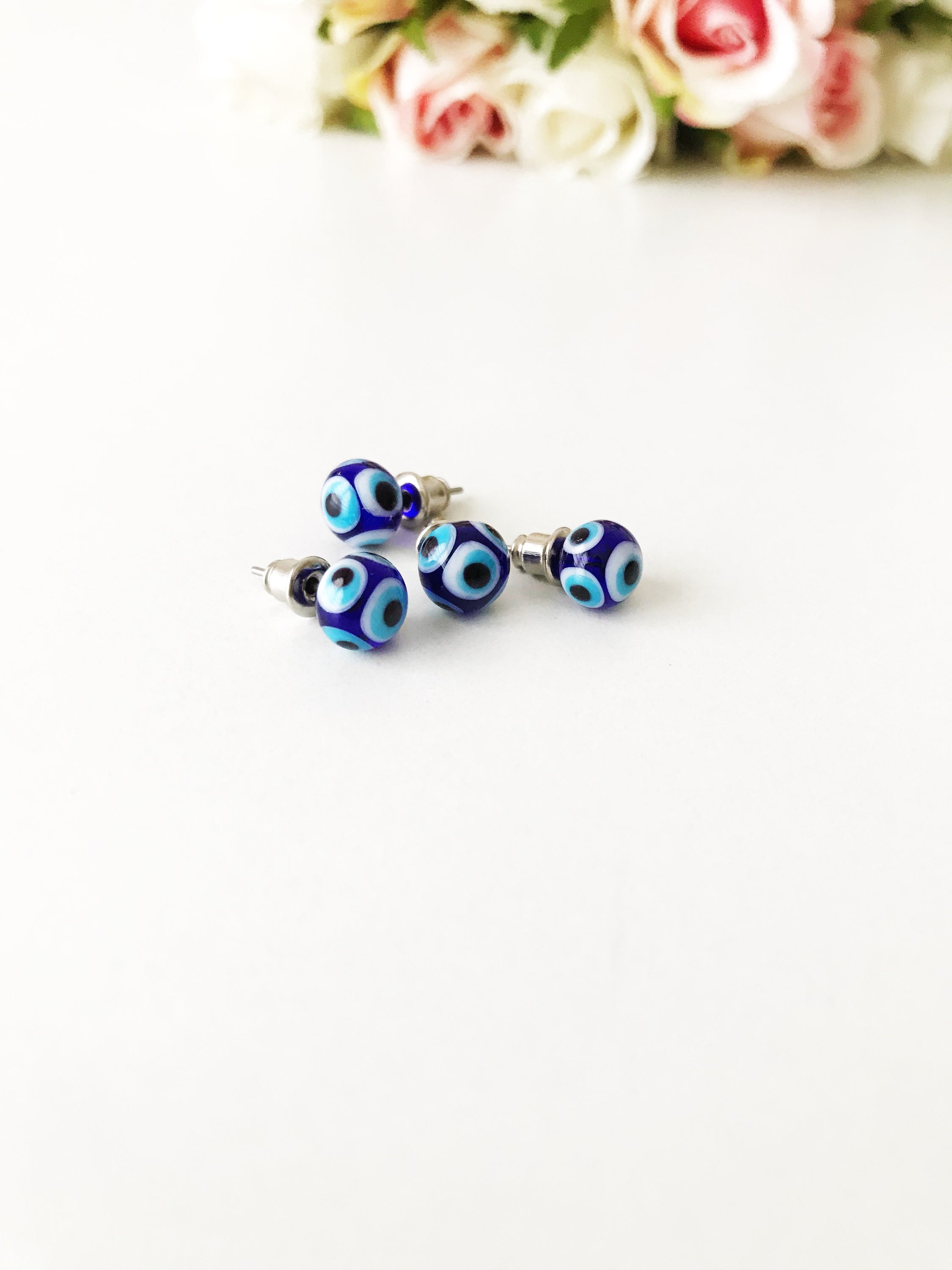 A pair of handmade glass evil eye stud earrings in dark blue and turquoise, symbolizing protection and good luck, displayed elegantly.