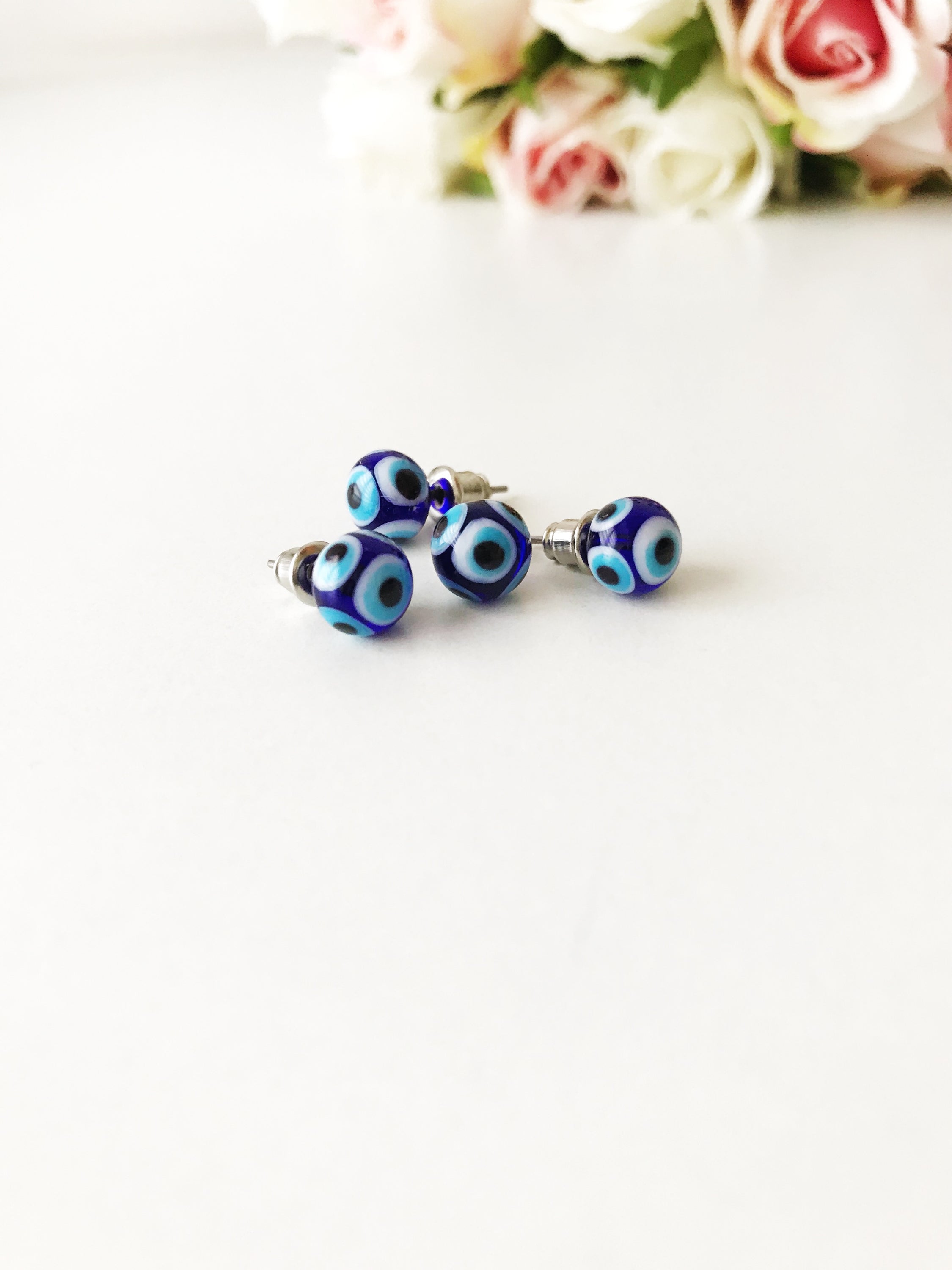 A pair of handmade glass evil eye stud earrings in dark blue and turquoise, symbolizing protection and good luck, displayed elegantly.