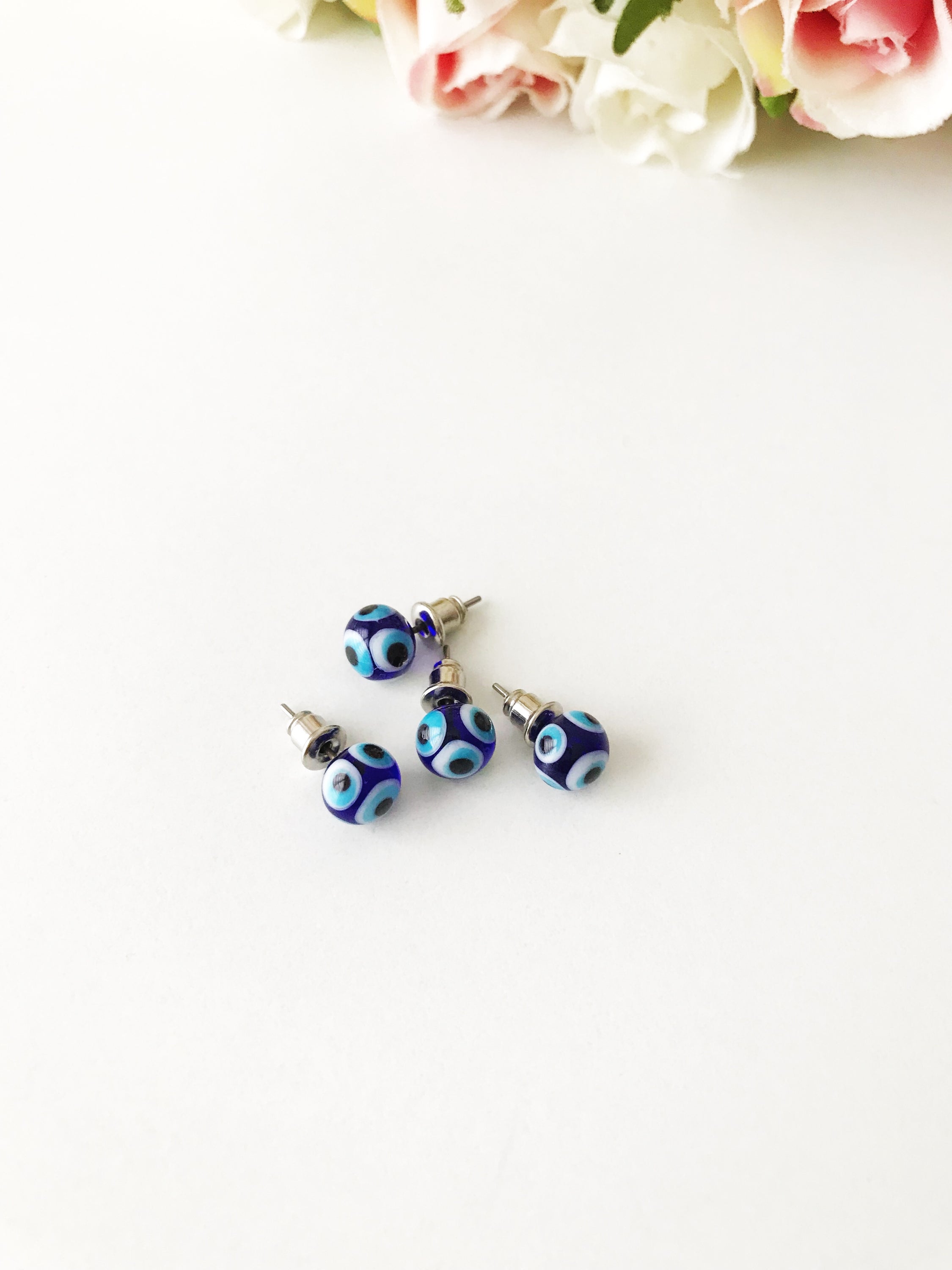 A pair of handmade glass evil eye stud earrings in dark blue and turquoise, symbolizing protection and good luck, displayed elegantly.