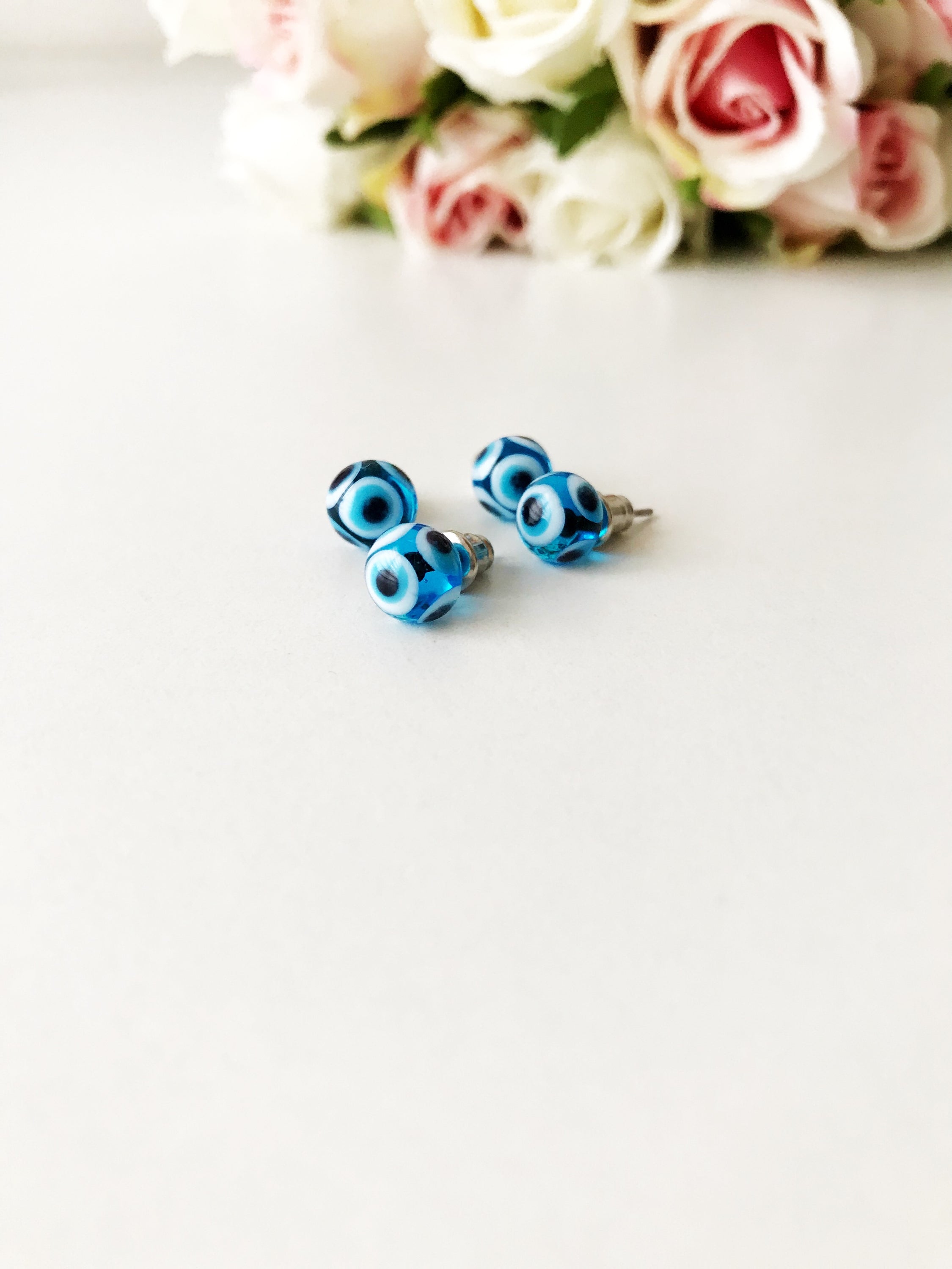 A pair of handmade glass evil eye stud earrings in dark blue and turquoise, symbolizing protection and good luck, displayed elegantly.