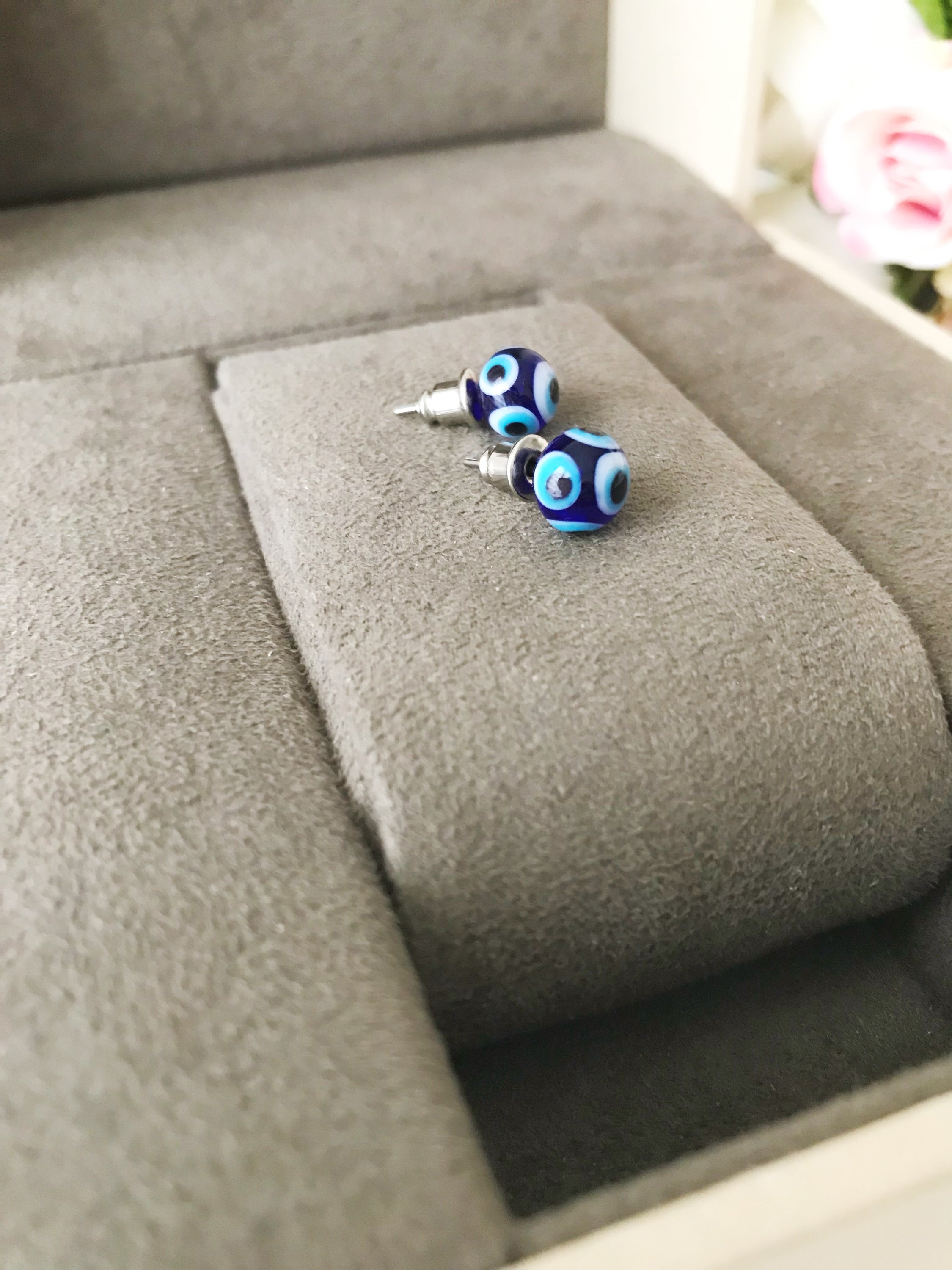 A pair of handmade glass evil eye stud earrings in dark blue and turquoise, symbolizing protection and good luck, displayed elegantly.